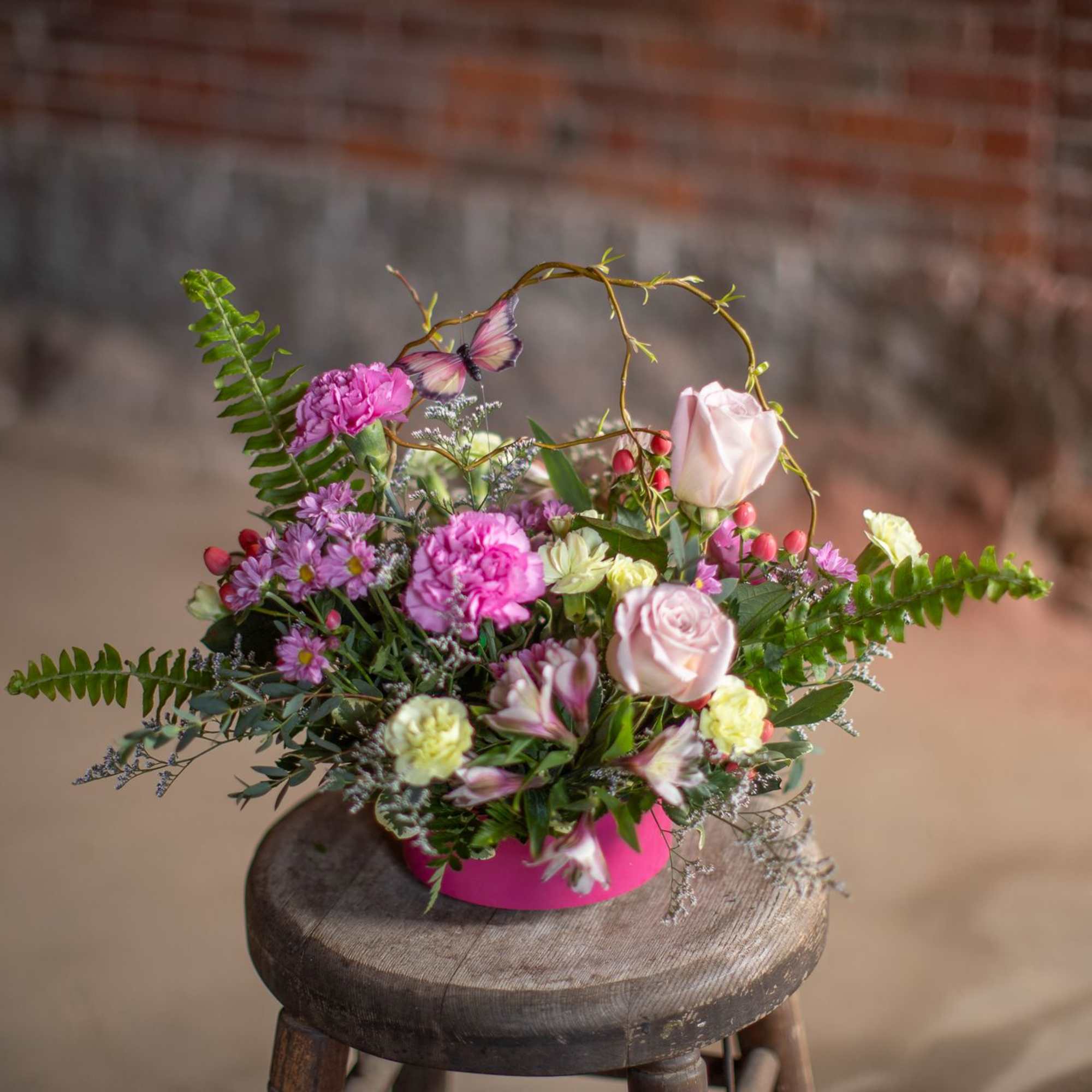 A butterfly dances through woven curly willow branches and festive seasonal blooms