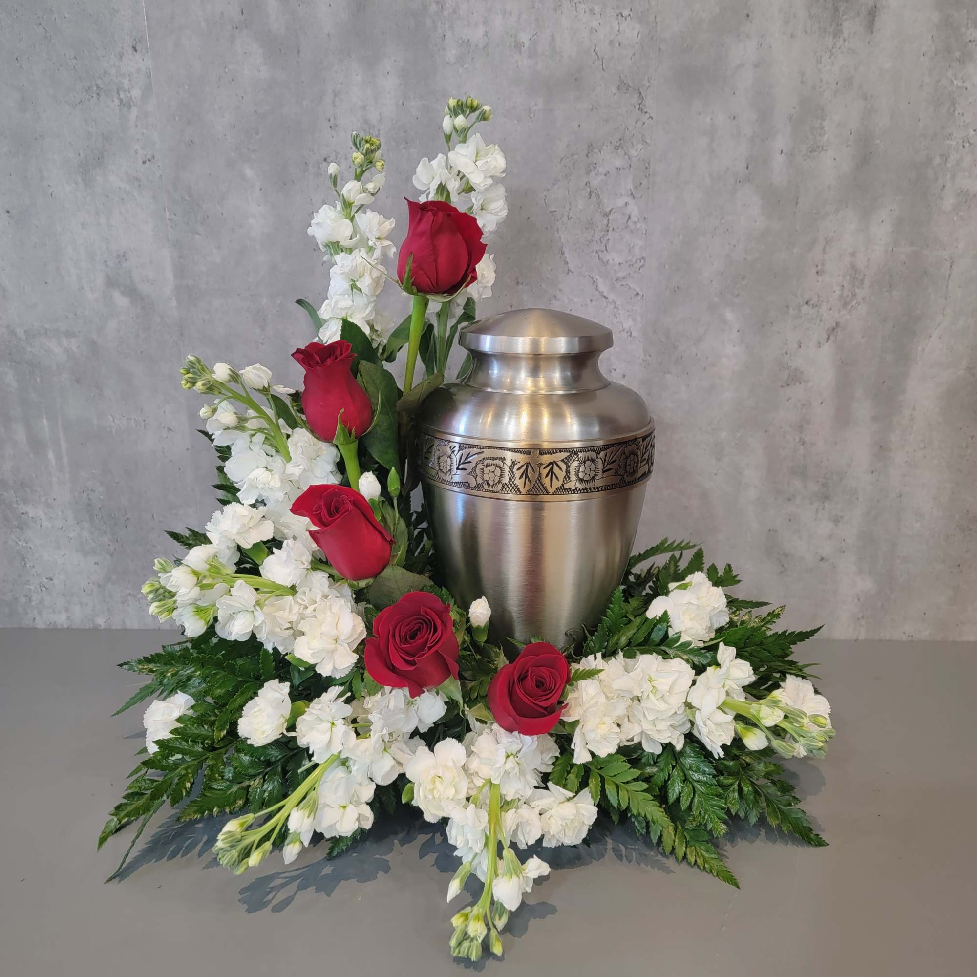Red roses and white flowers arranged around a silver urn.