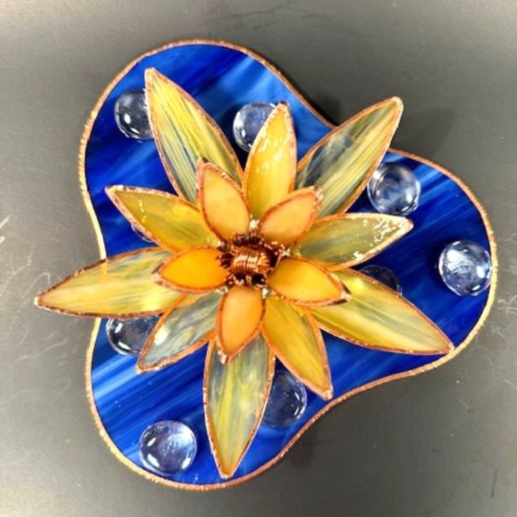 A sunlit, sculptural flower in warm yellow and orange stained glass catches
