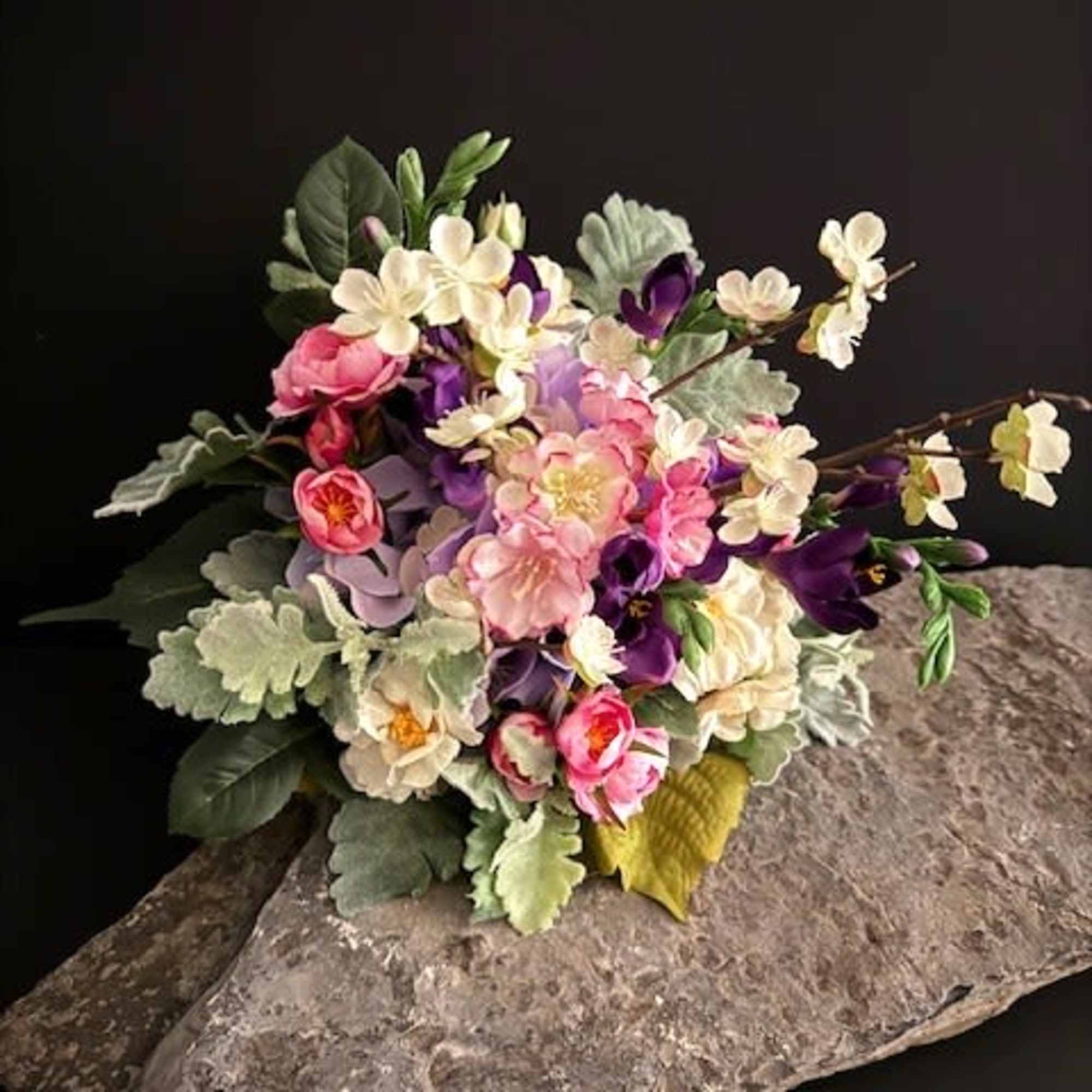 A compact dome of soft pink, cream, lavender and purple silk blooms