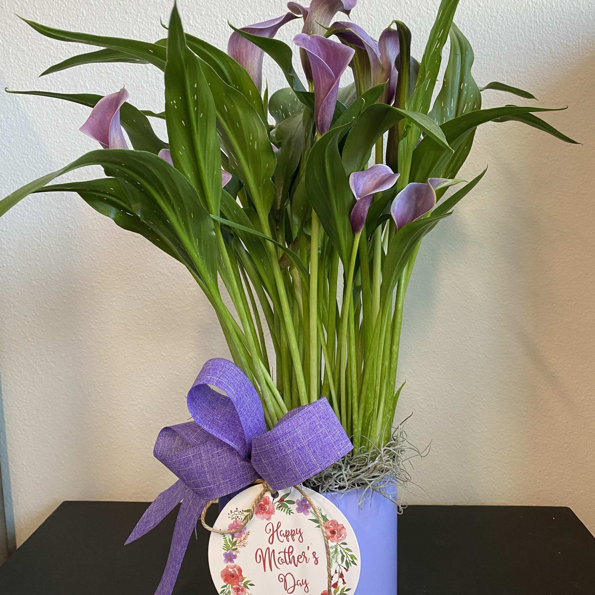 Purple calla lilies in a lavender pot with a purple ribbon and Mother's Day tag