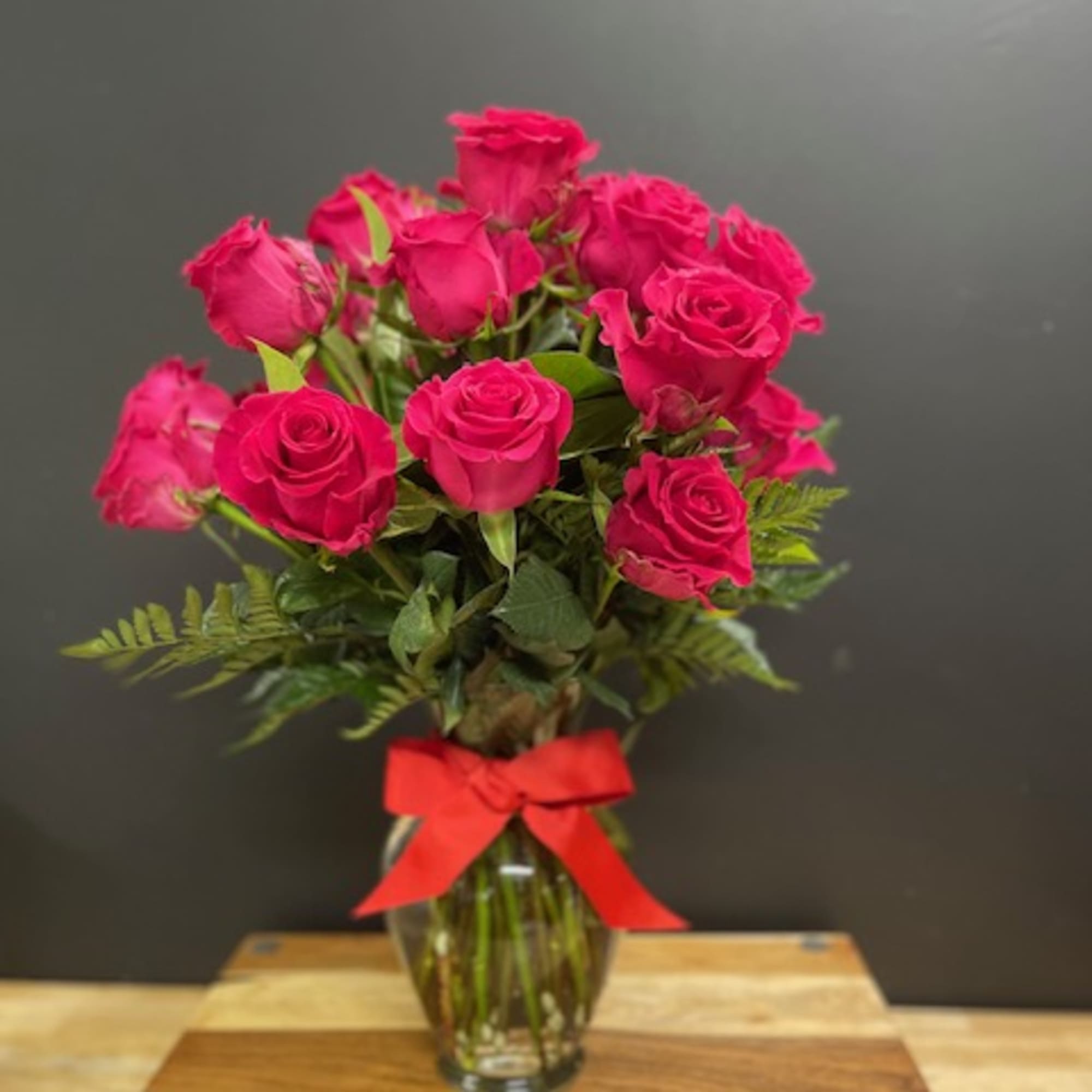Tall bouquet of hot pink roses in a clear glass vase with a red bow