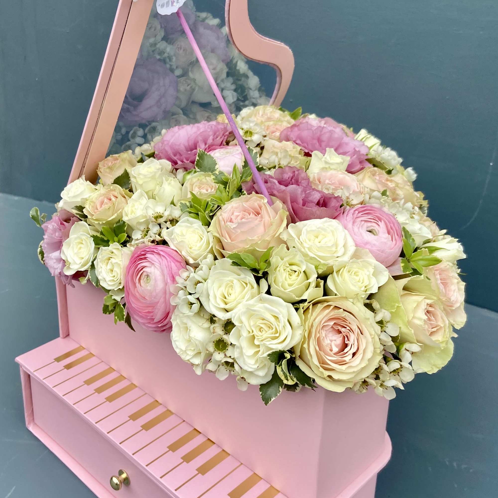 Pink piano-shaped flower box with cream and pink roses and ranunculus topped with a butterfly decoration