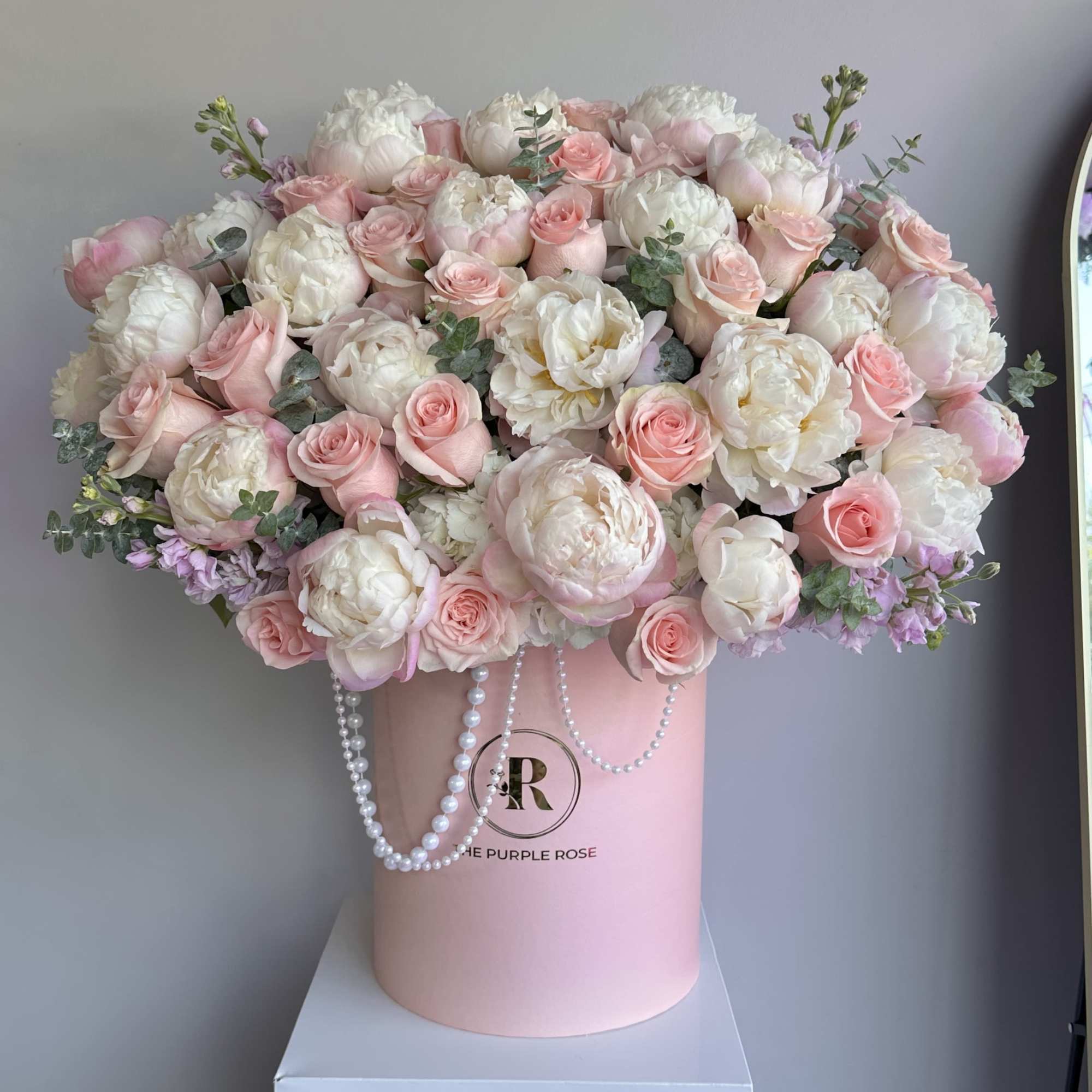 Large blush pink and white peony and rose arrangement in a pink hat box with pearl strands.