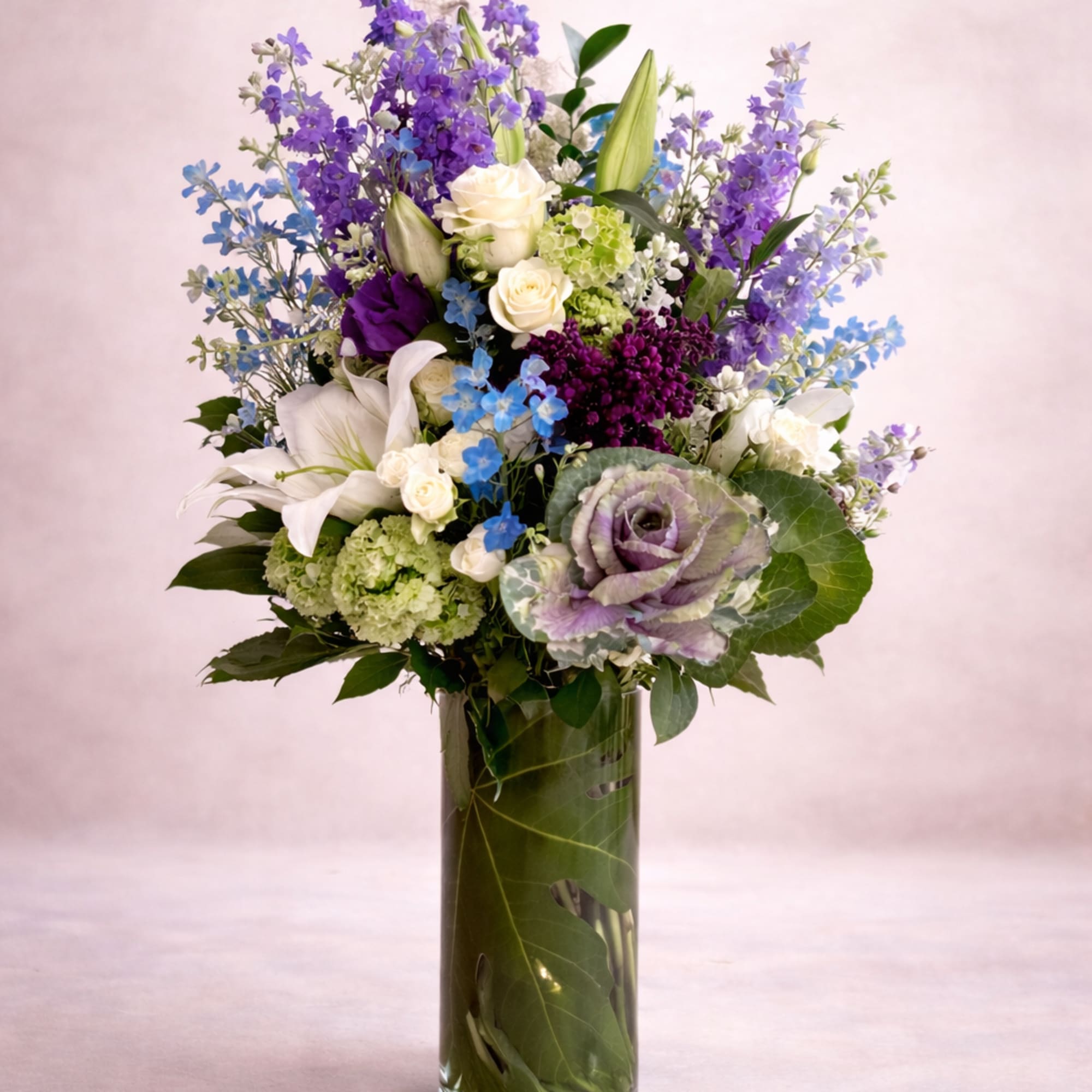 A tall, airy garden-style arrangement rises gracefully from a clear cylinder vase