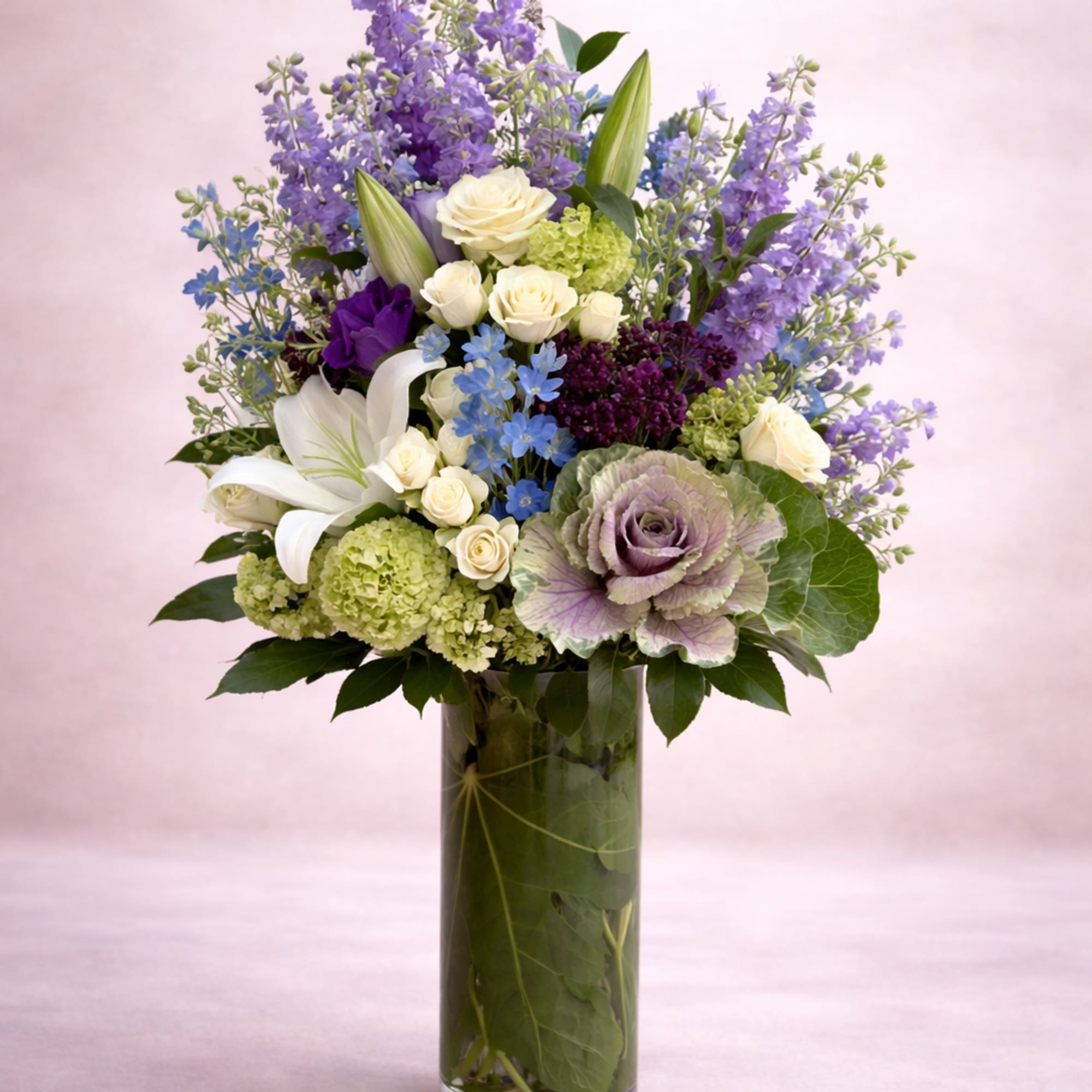 A tall, airy garden-style arrangement rises gracefully from a clear cylinder vase