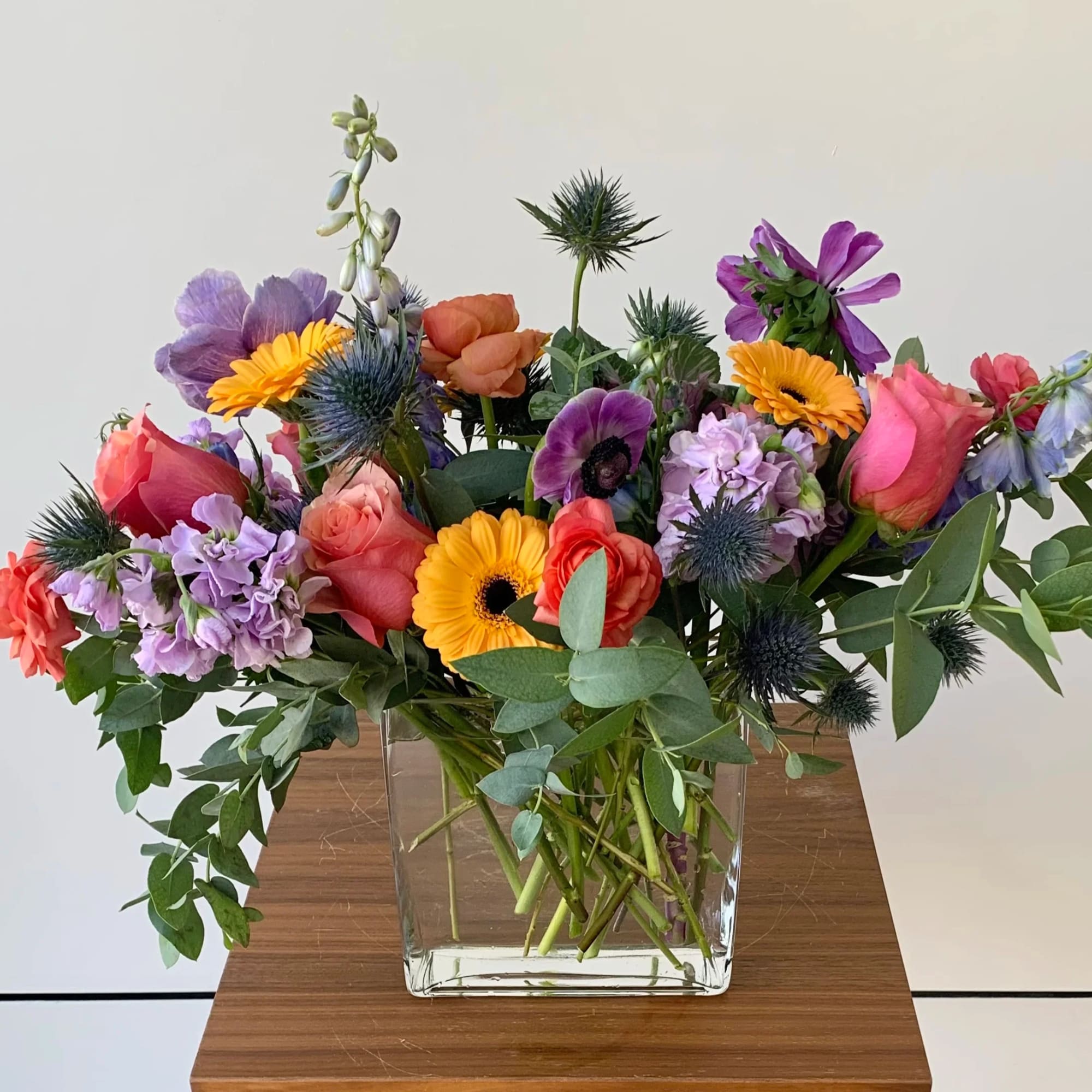 Mixed bouquet of roses, gerbera daisies, and purple blooms in a glass vase