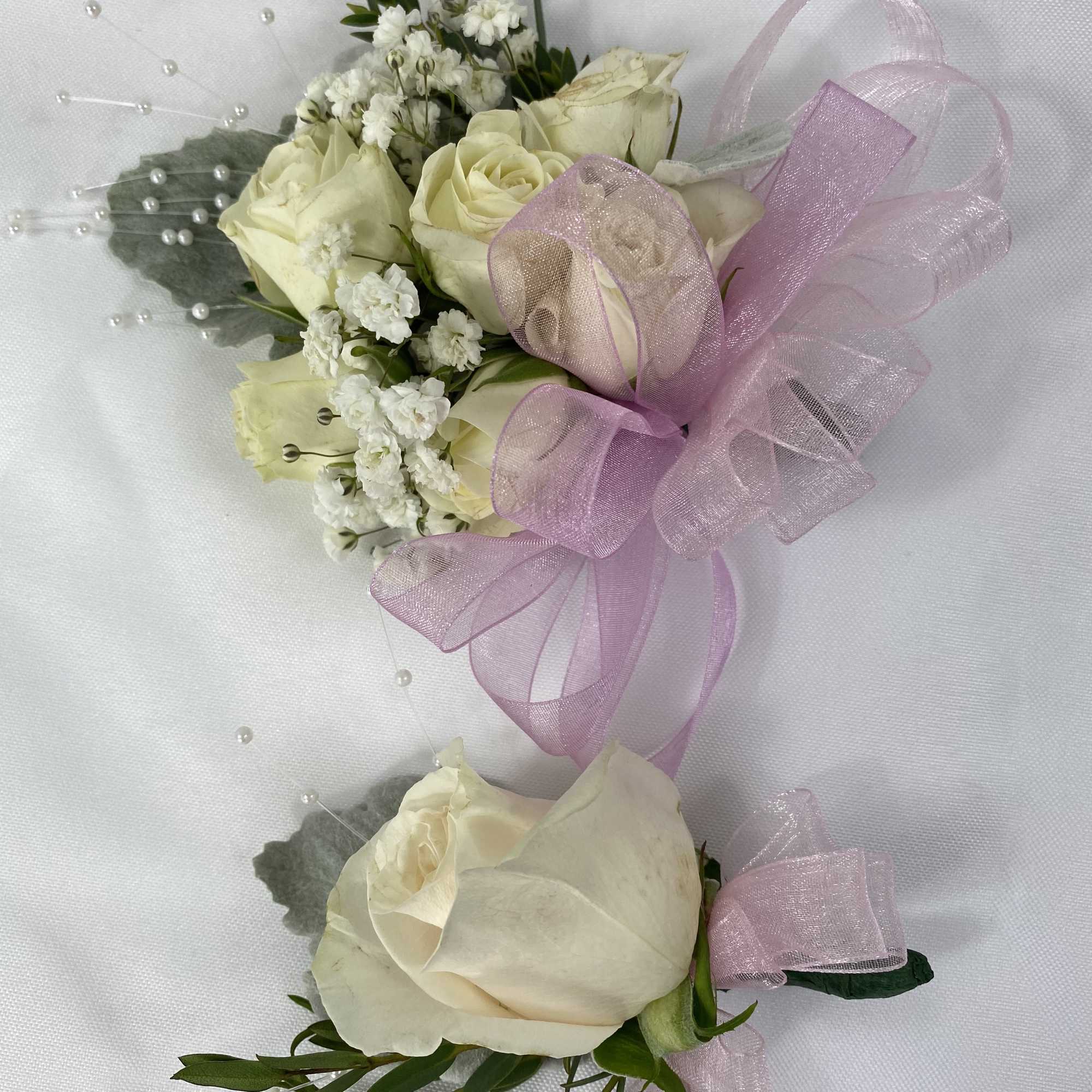 Two white rose boutonnieres with pink ribbon and pearl accents