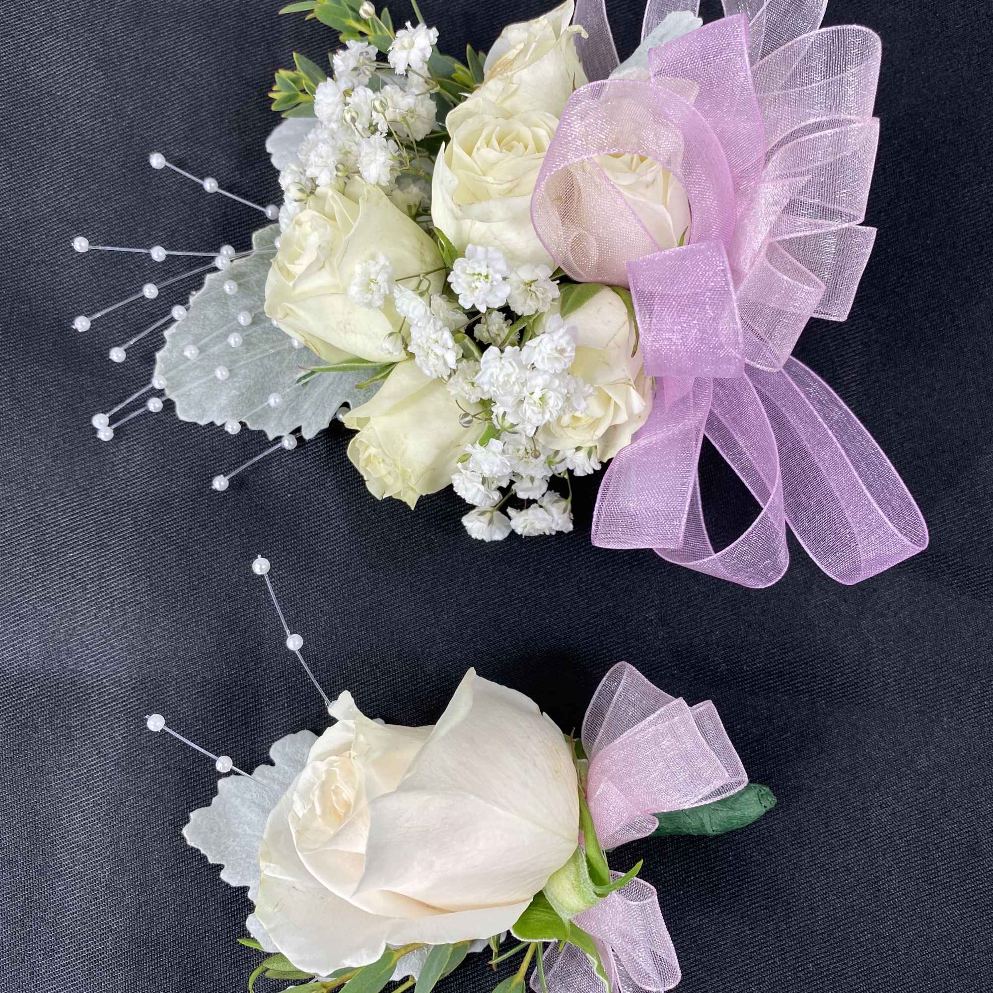 Two white rose corsages with pink ribbon and pearl accents