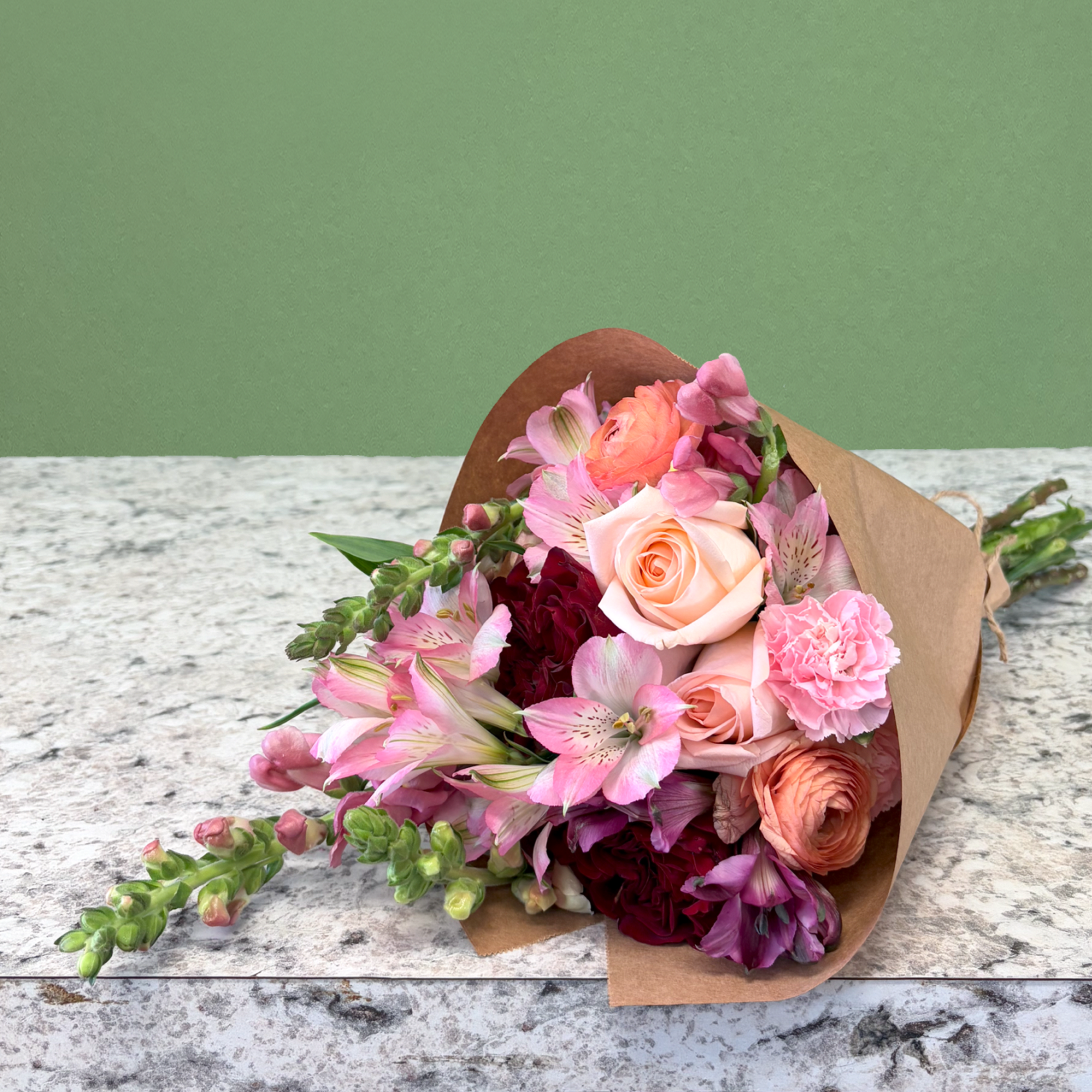 Kraft-wrapped bouquet with peach roses, pink alstroemeria, and burgundy flowers on a stone surface