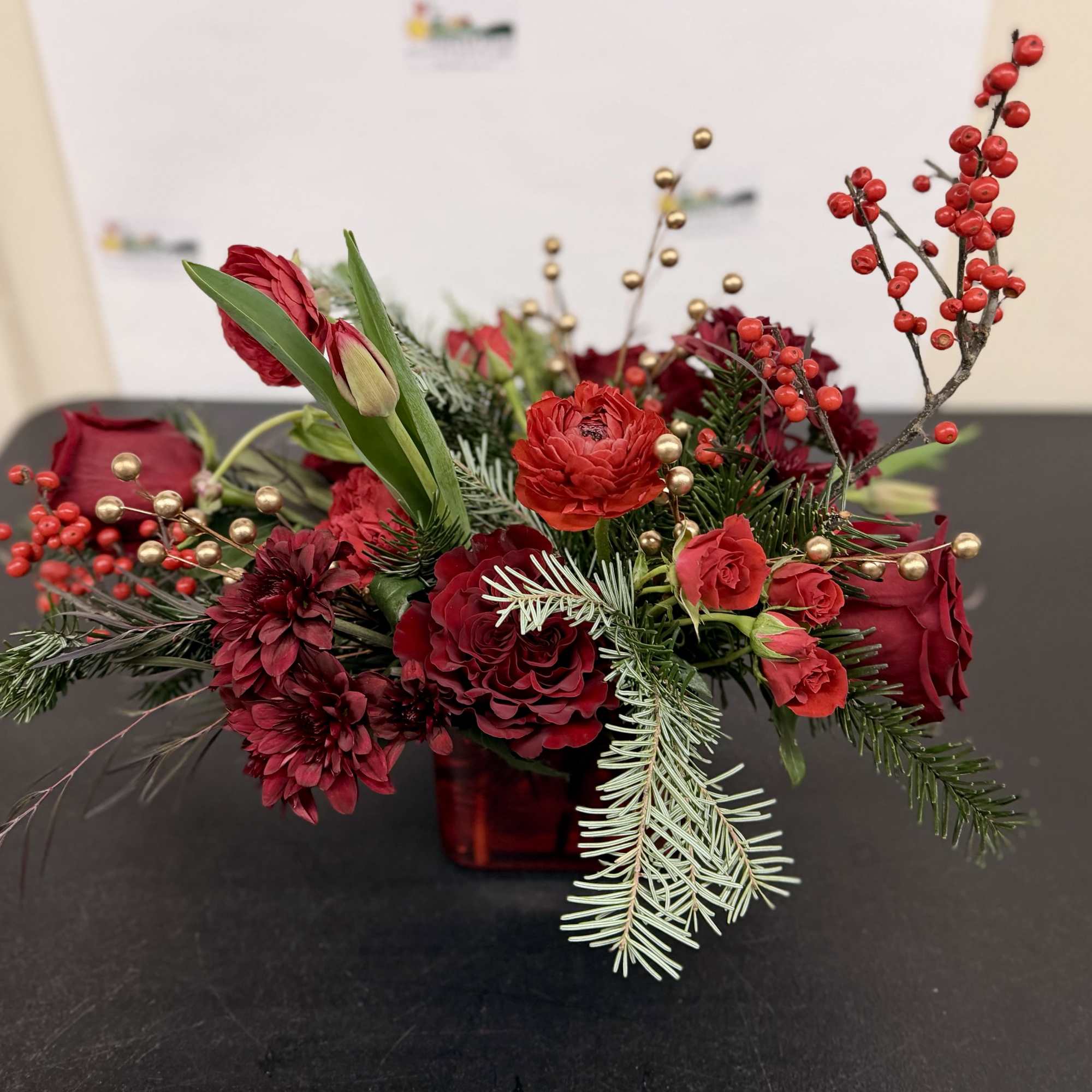 Red floral arrangement in a square glass vase with berries and evergreen accents