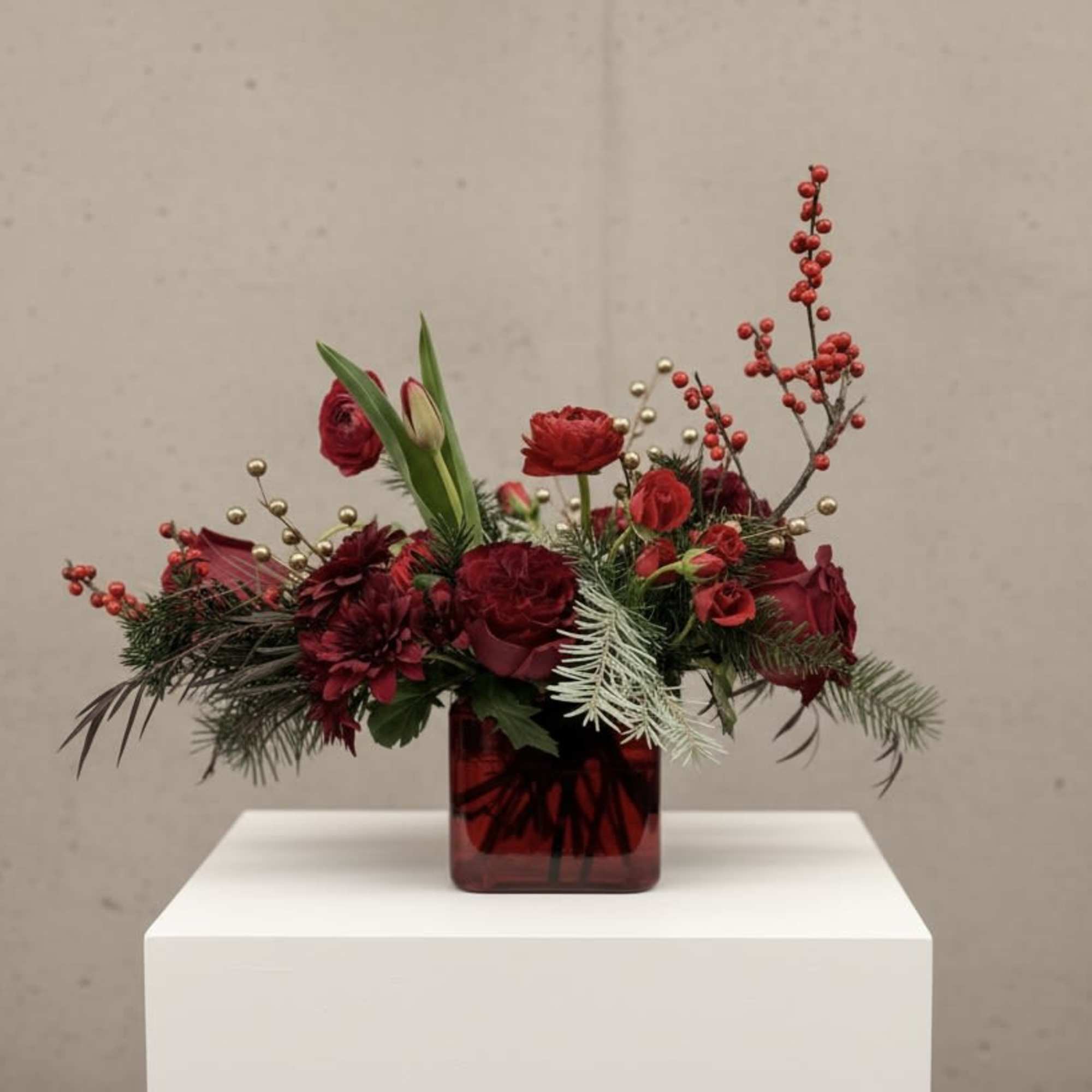 Red floral arrangement in a square glass vase with berries and greenery