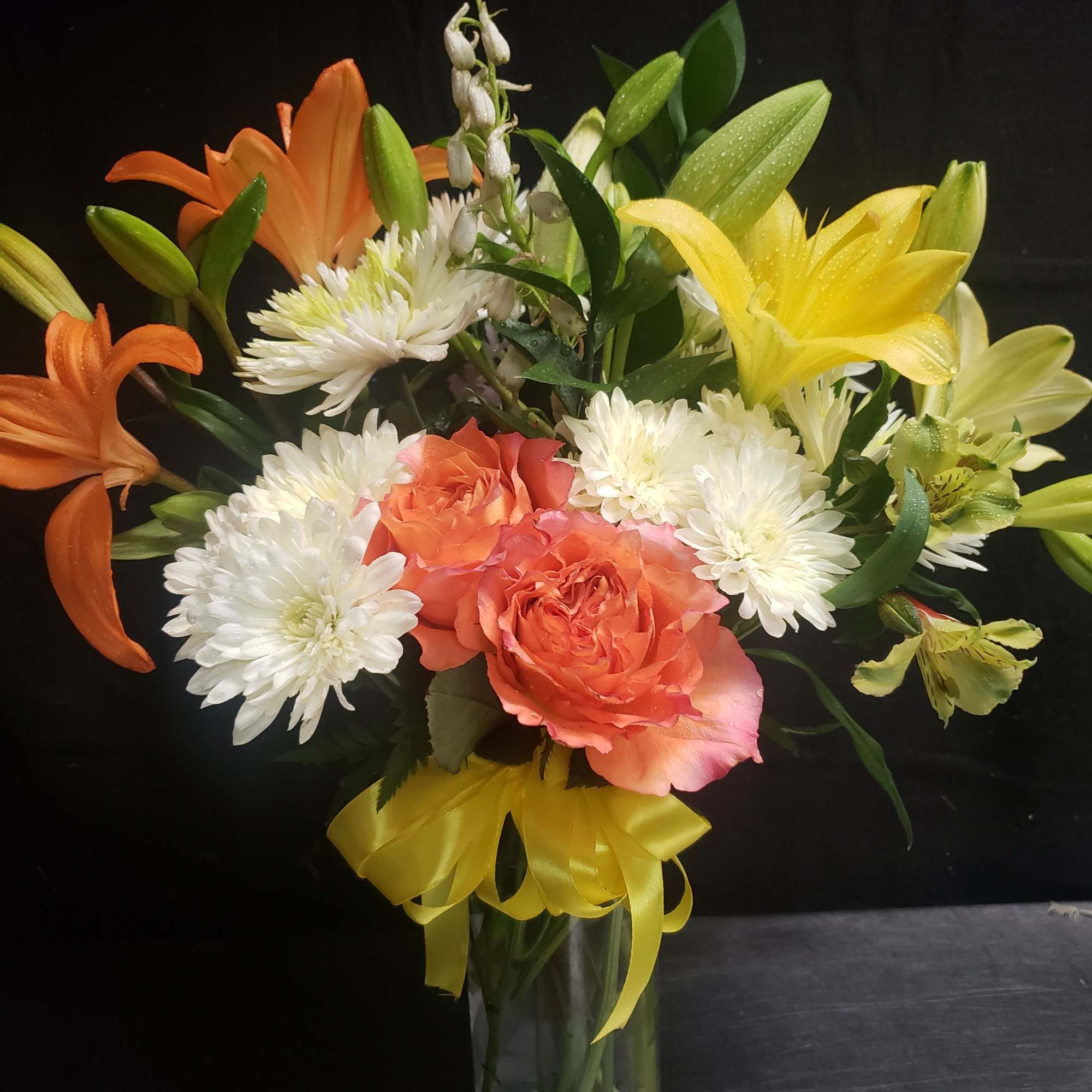 Bright citrus tones of orange roses and yellow lilies make this flower