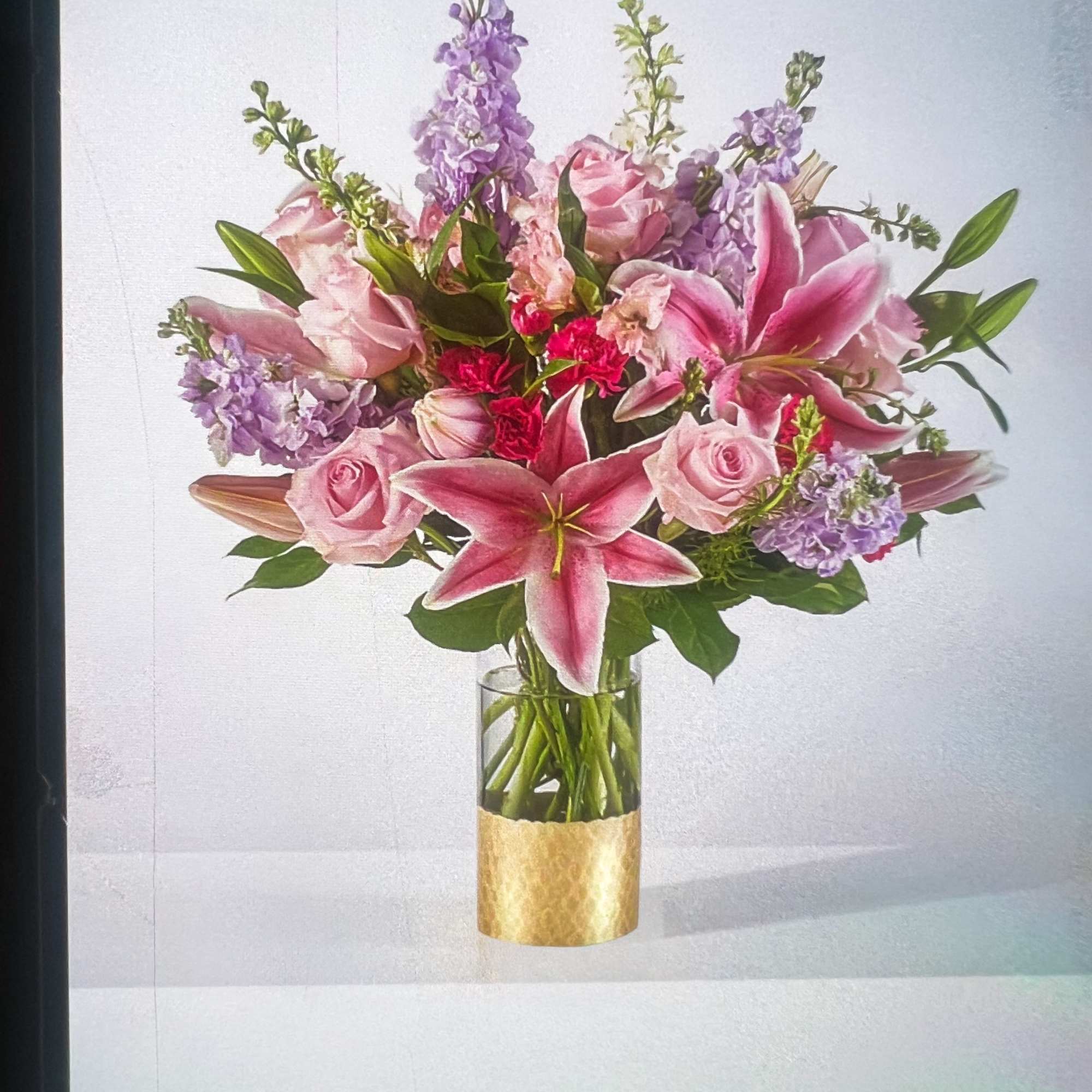 Pink lilies and roses in a clear glass vase with a gold wrap