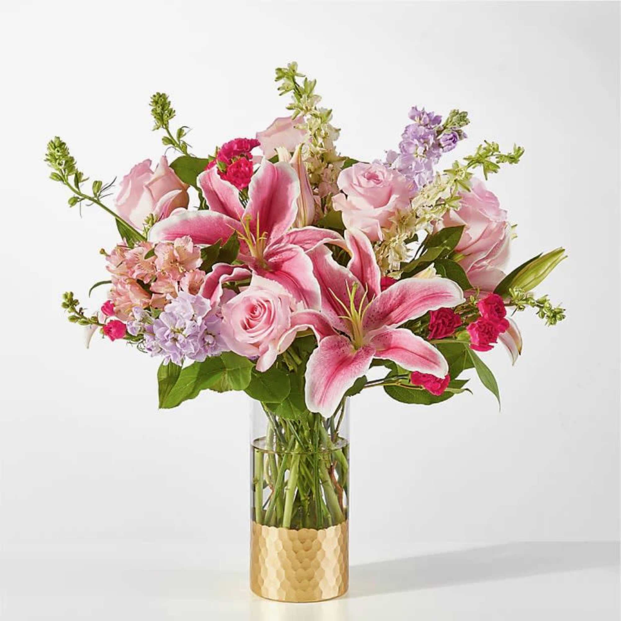Pink lilies and roses in a clear glass vase with a gold base