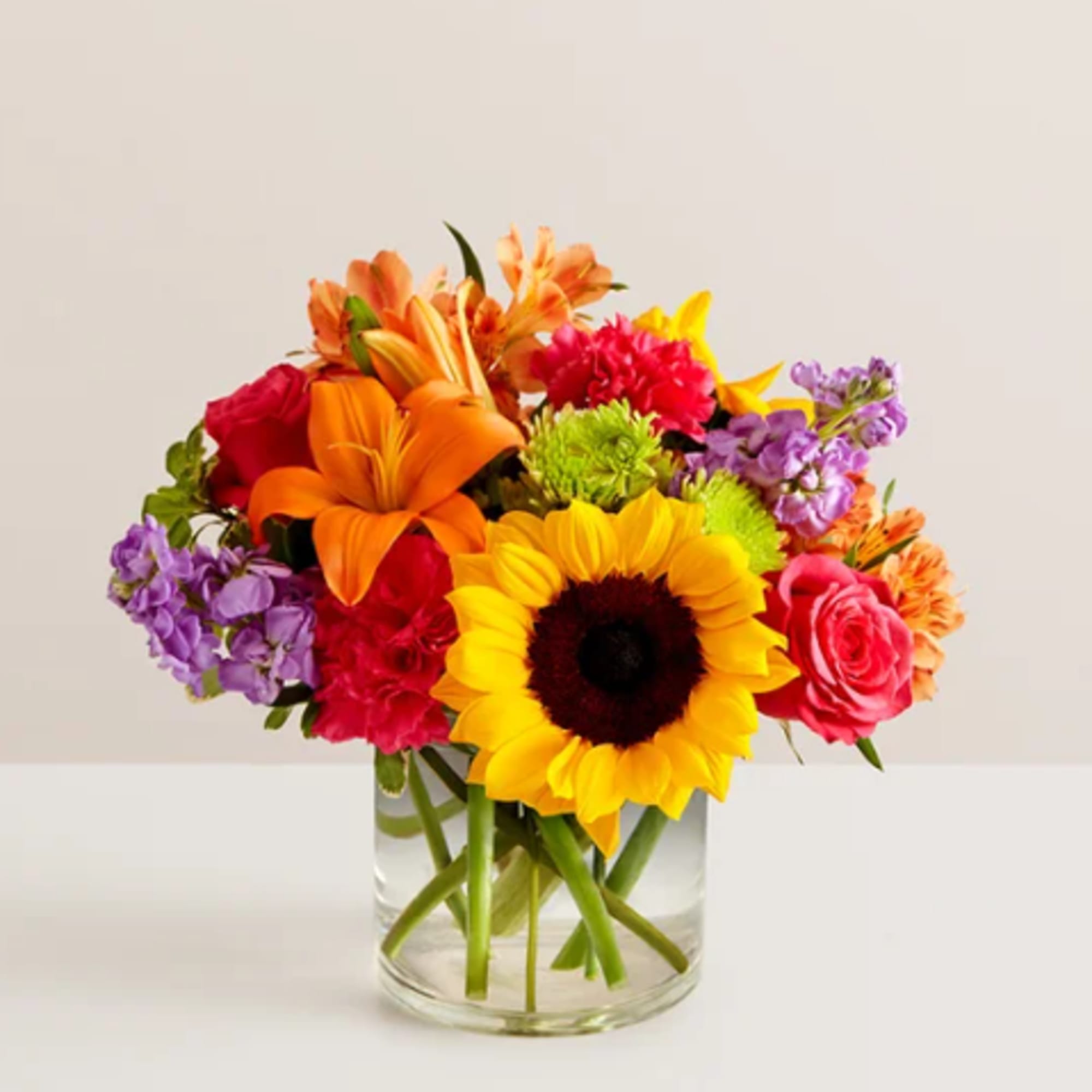 Colorful mixed bouquet in a clear glass vase with a sunflower and lilies