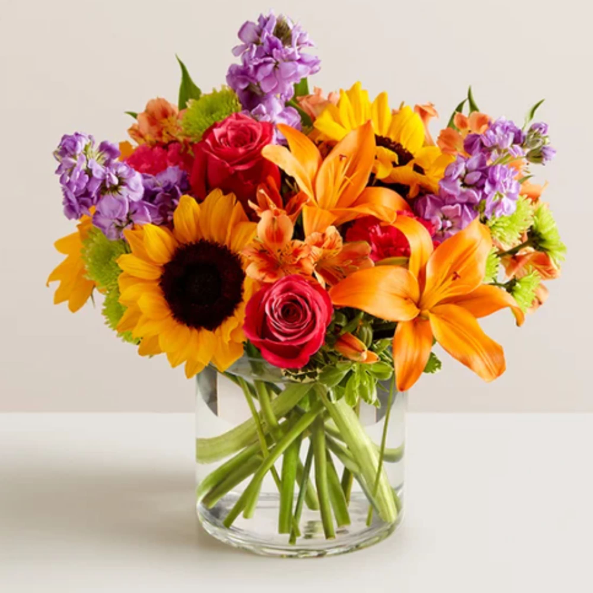 Mixed bouquet of sunflowers, roses, lilies, and purple flowers in a glass vase
