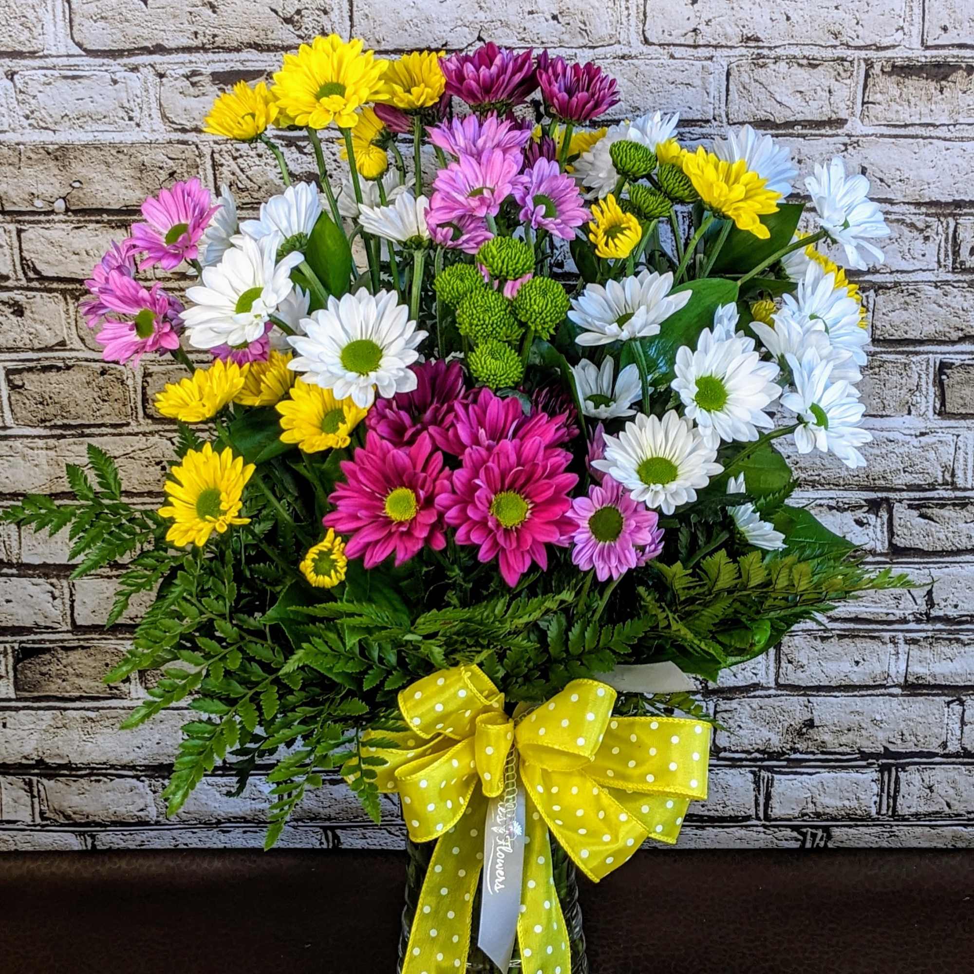 Mixed daisy bouquet in a glass vase with a yellow polka-dot ribbon
