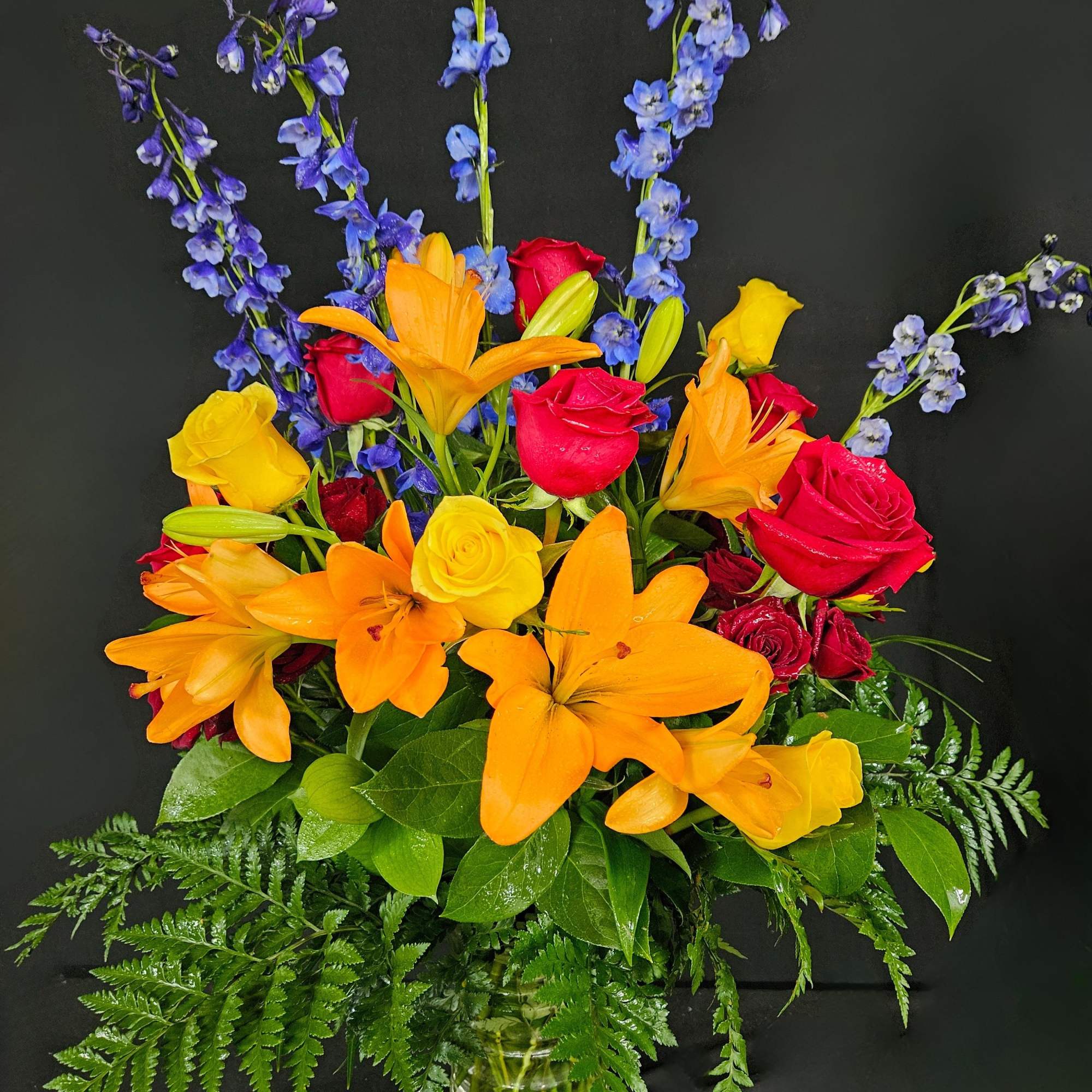 Bright mixed bouquet of orange lilies, red and yellow roses in a glass vase