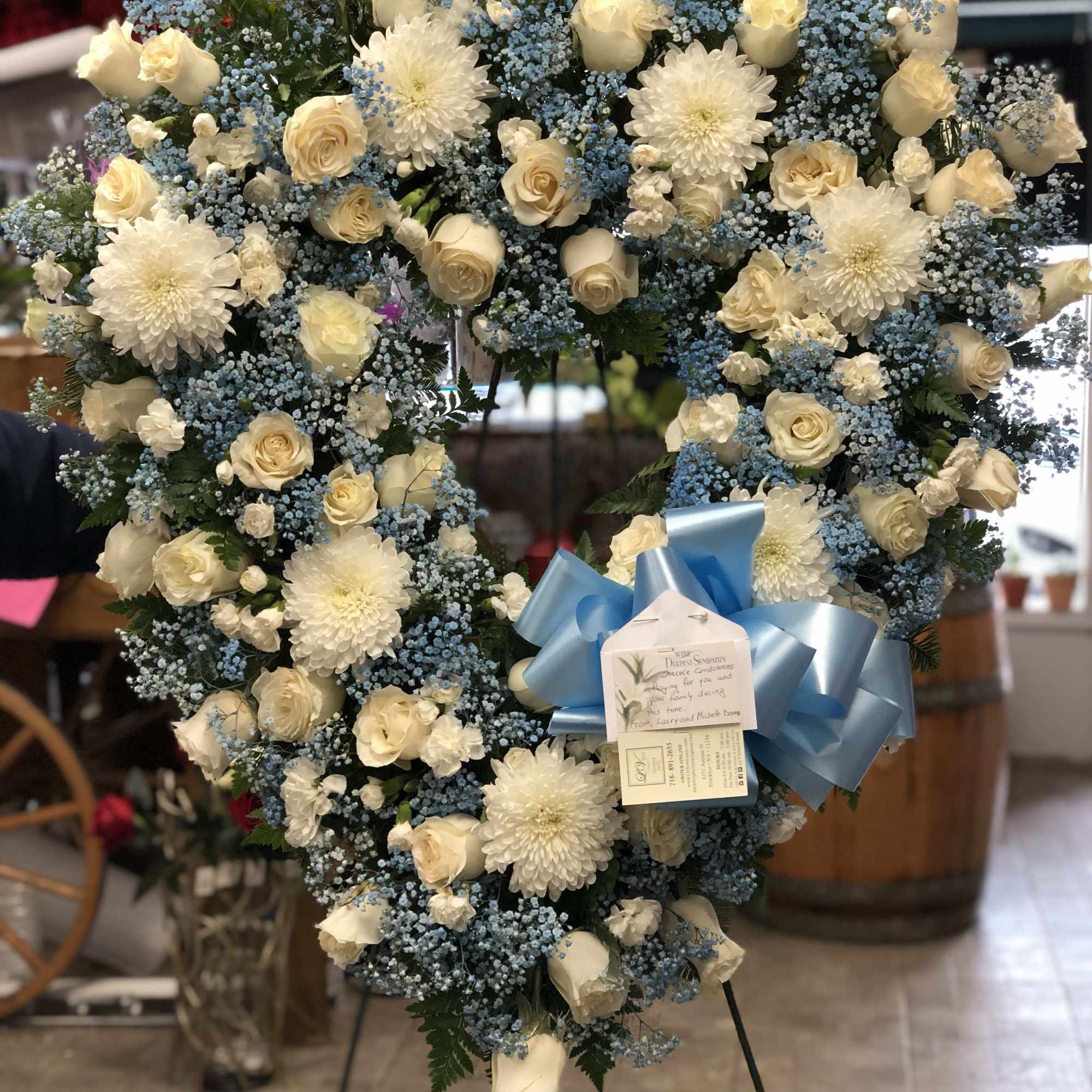 Heart-shaped floral wreath with white roses and chrysanthemums accented by blue filler flowers