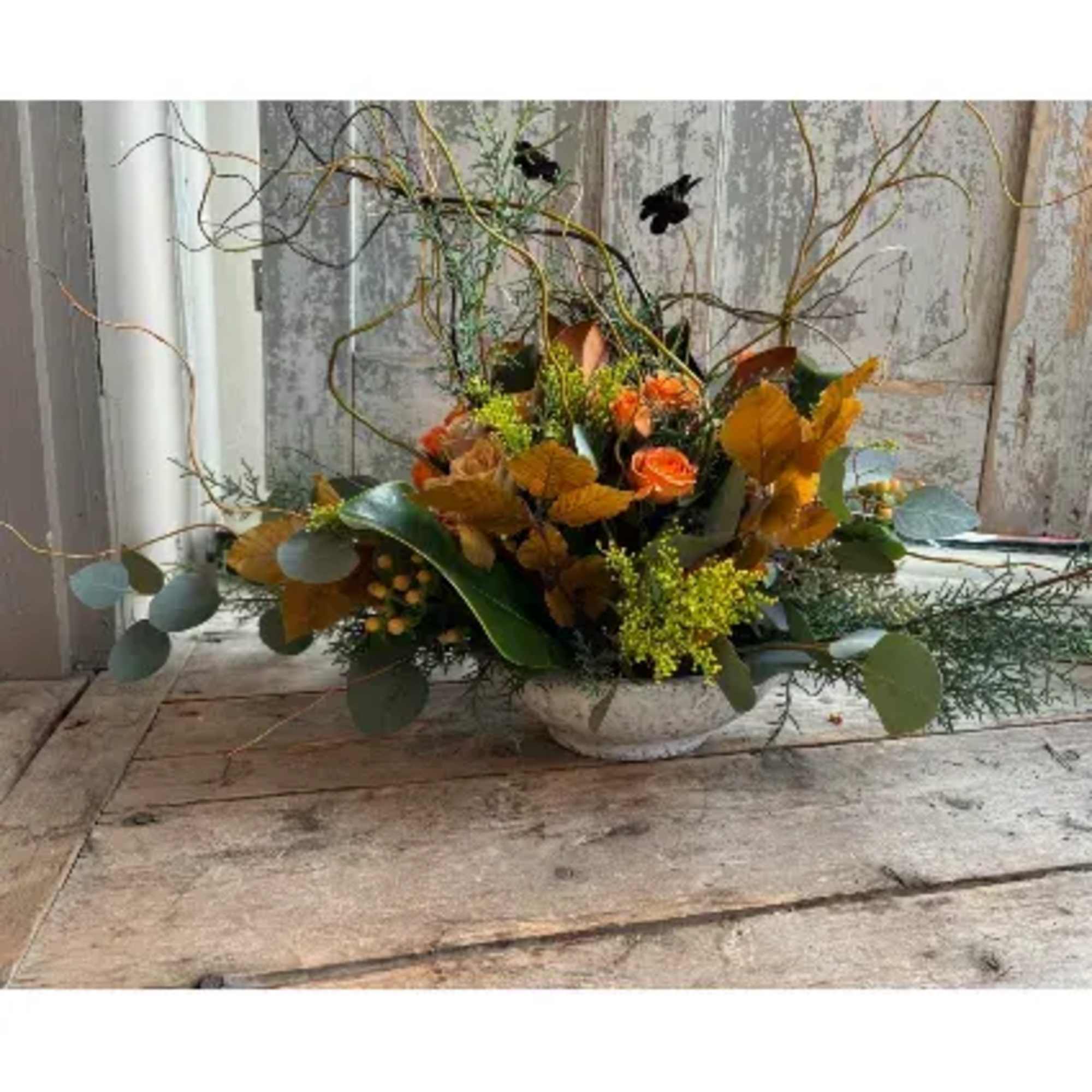 Seasonally colored roses, berries, and foliage are presented in a stoneware bowl