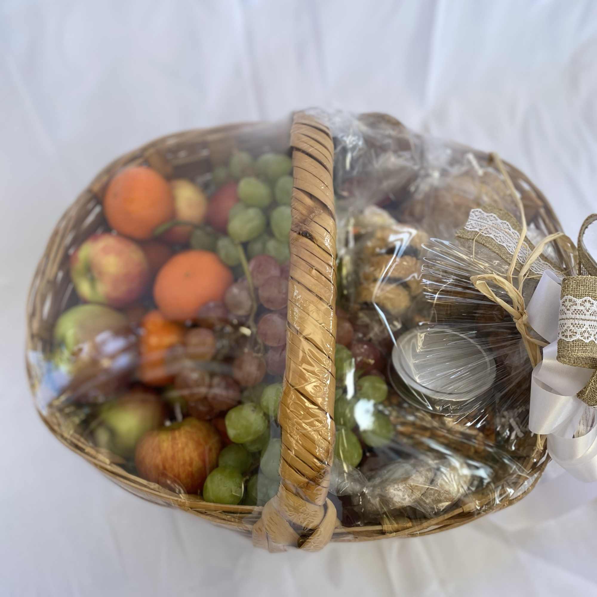 Large wicker gift basket wrapped in plastic with assorted fruits and packaged treats.