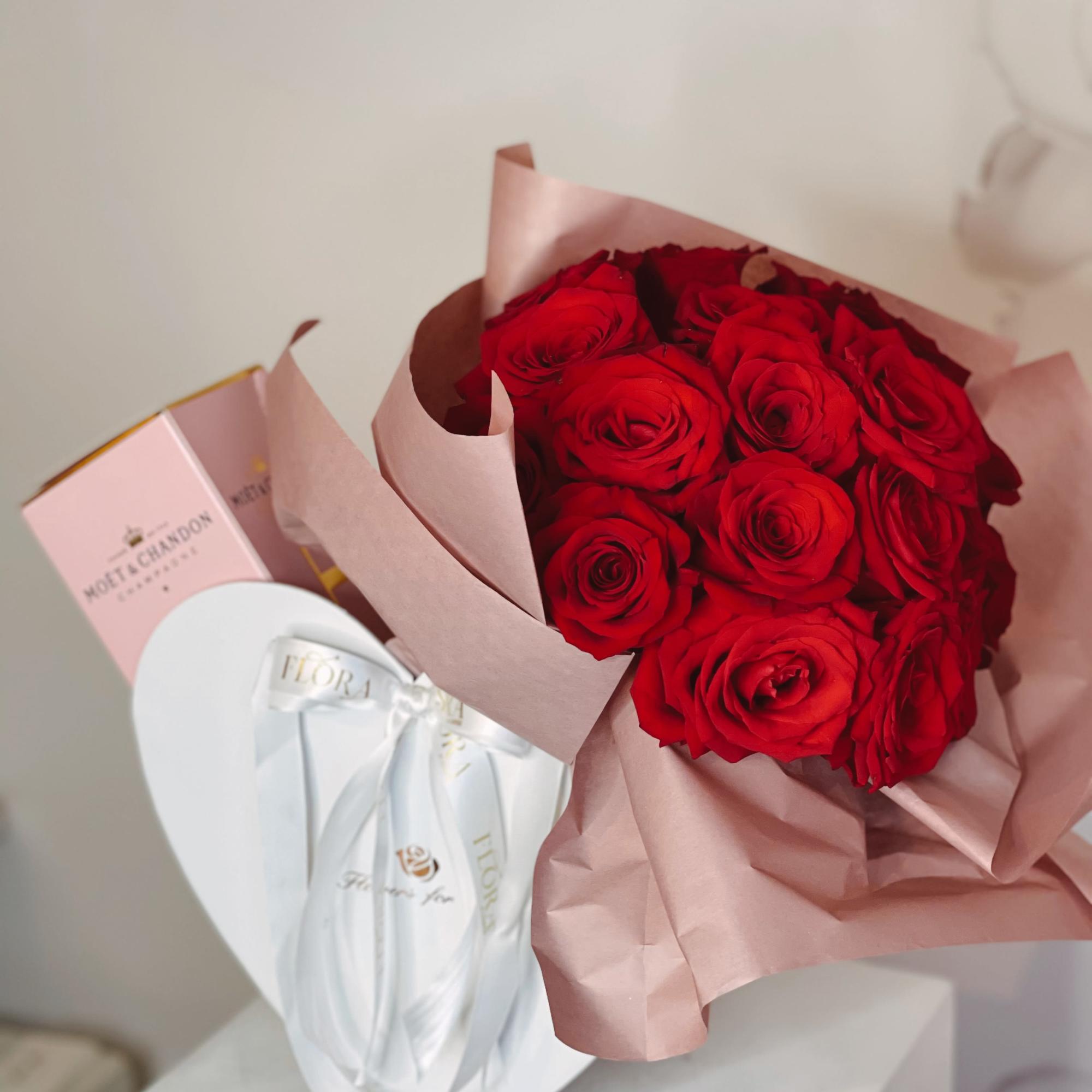 Bouquet of red roses wrapped in pink paper with a gift box beside it