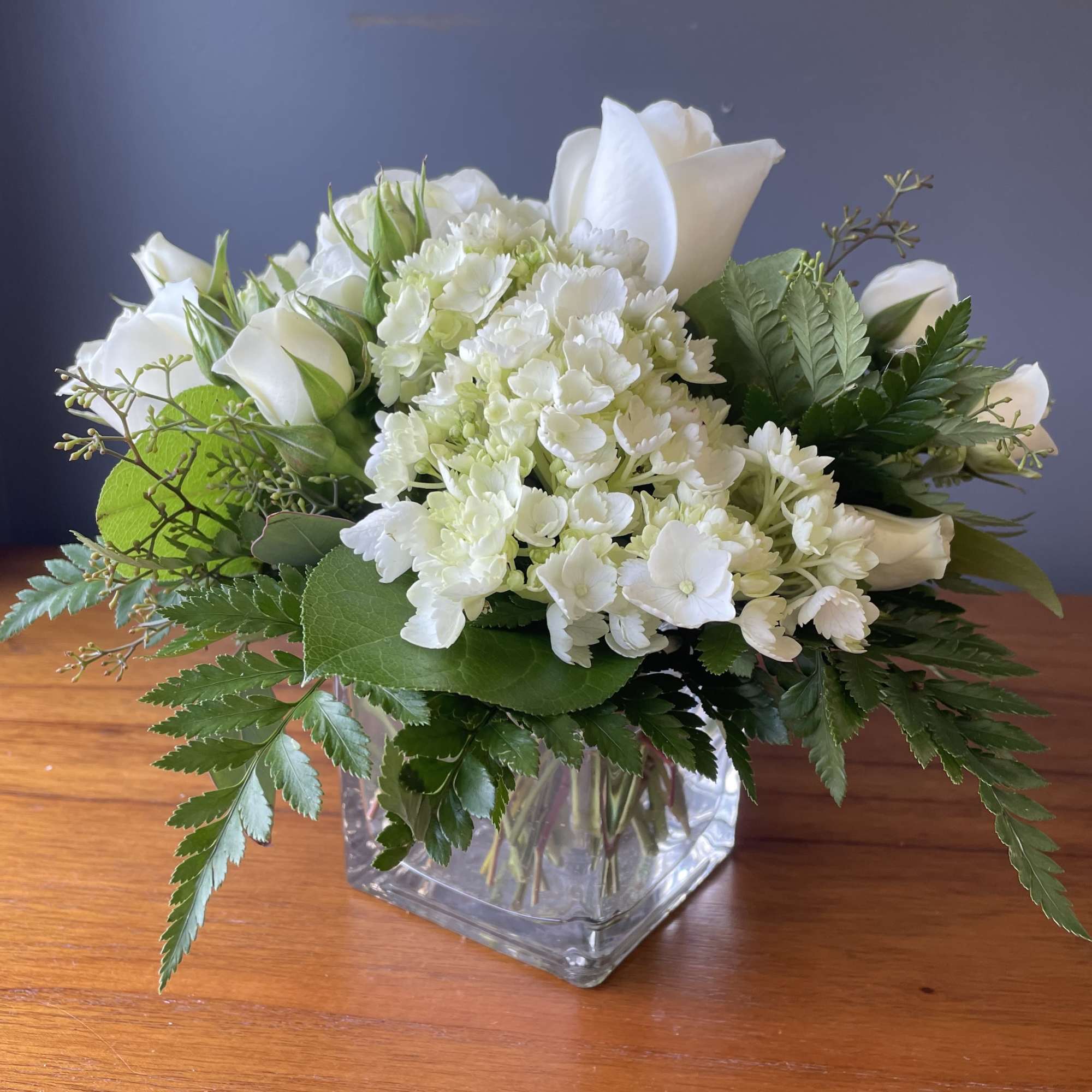 Low arrangement of white roses and hydrangeas in a clear glass cube vase