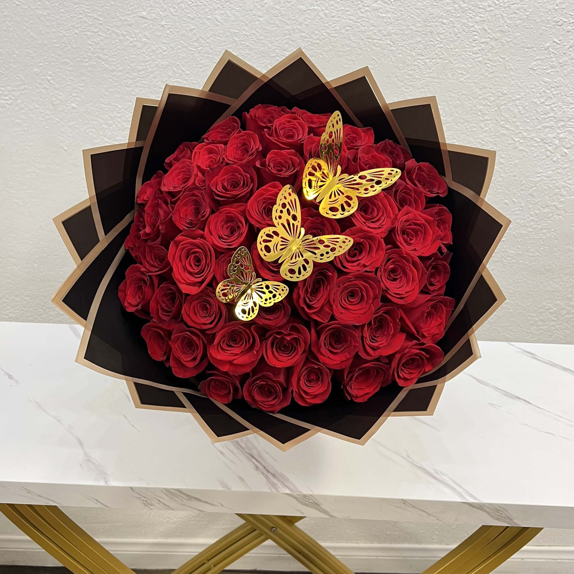 Bouquet of red roses wrapped in black paper with gold butterfly accents
