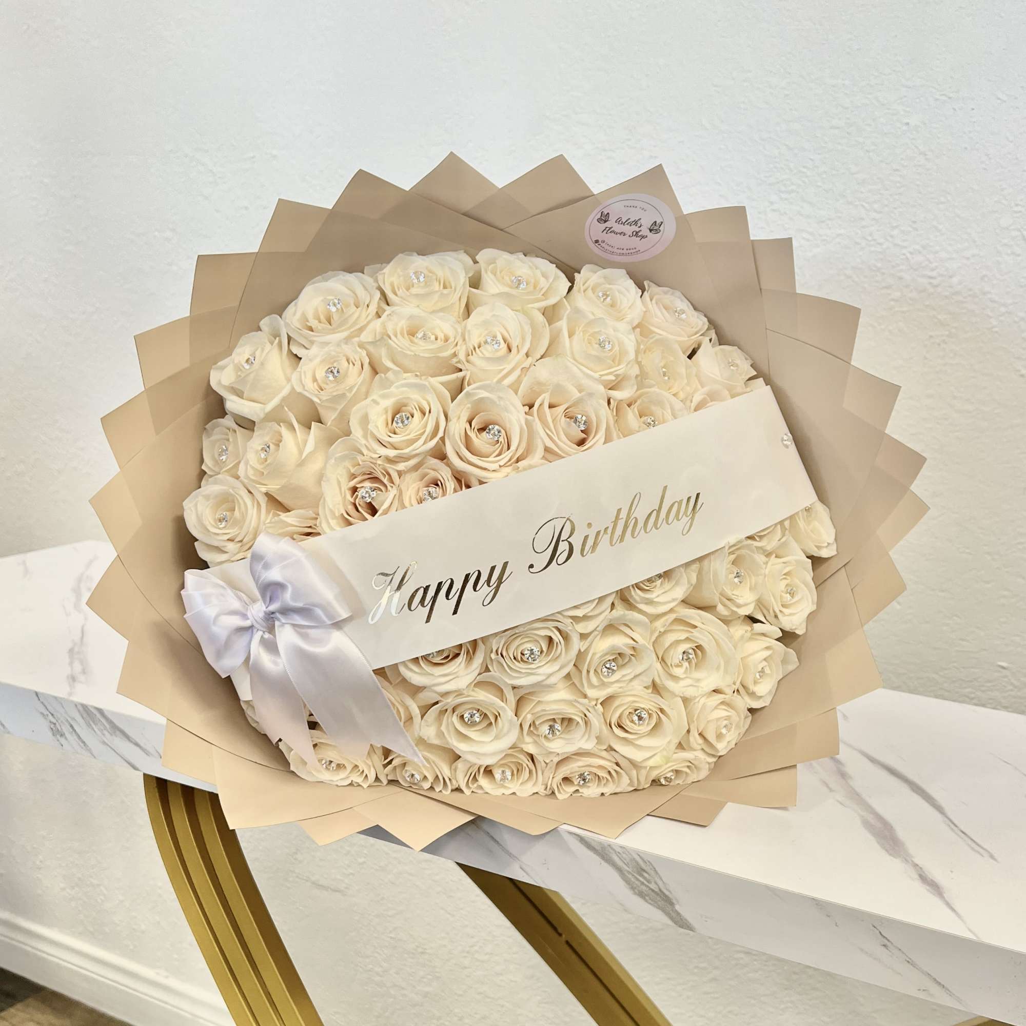 Cream rose bouquet wrapped in beige paper with a Happy Birthday banner