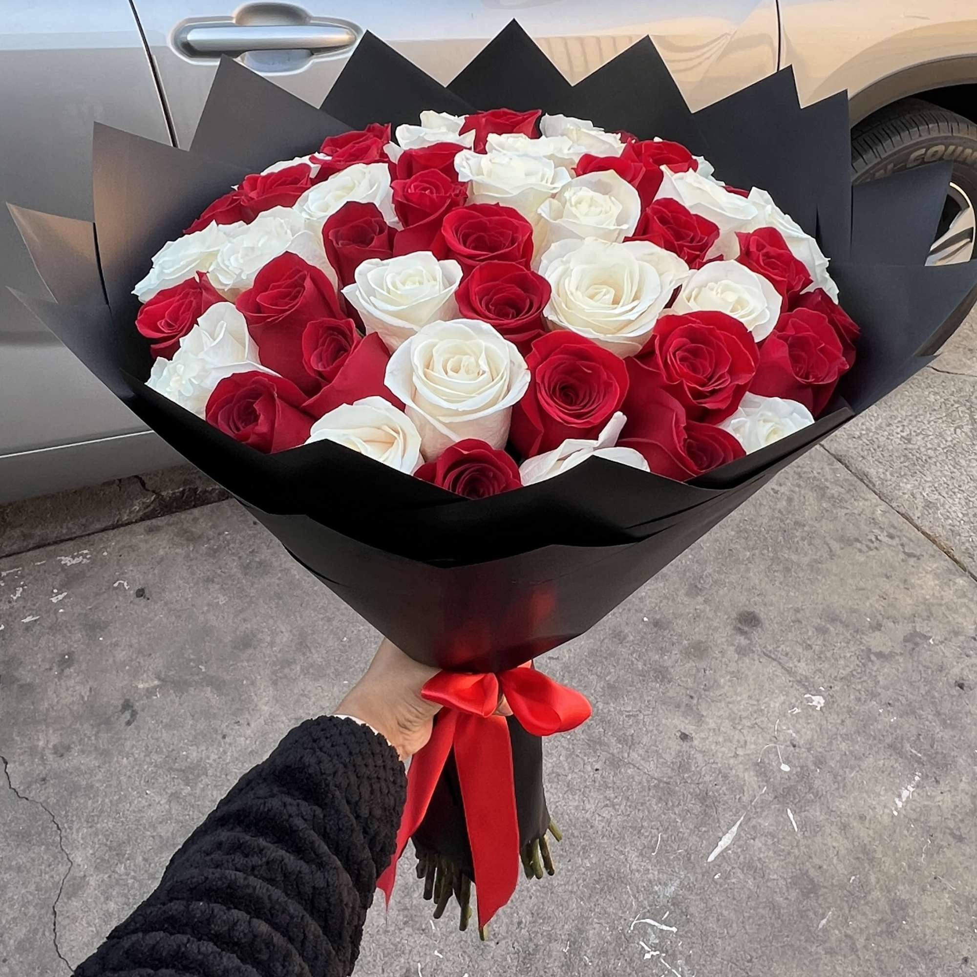 Large bouquet of red and white roses wrapped in black paper with a red ribbon