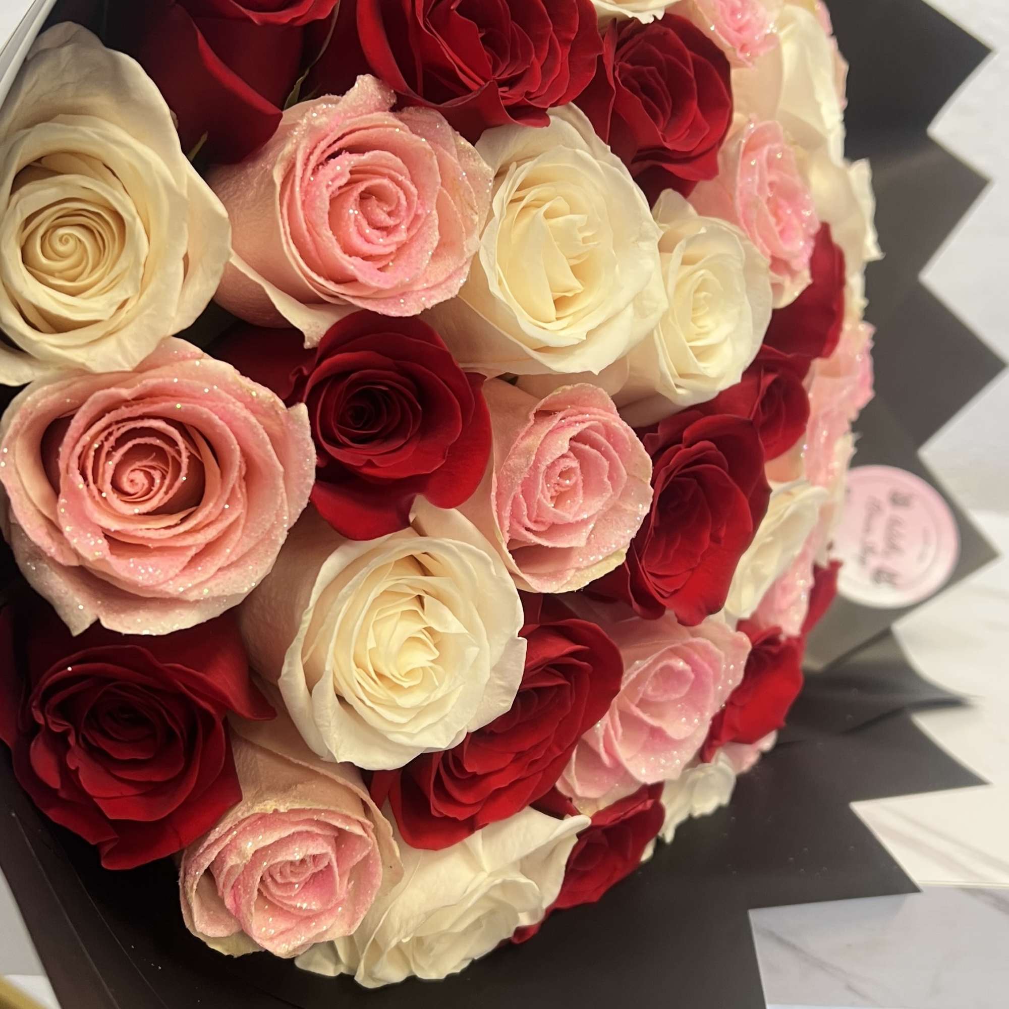 Bouquet of red, pink, and cream roses wrapped in black paper
