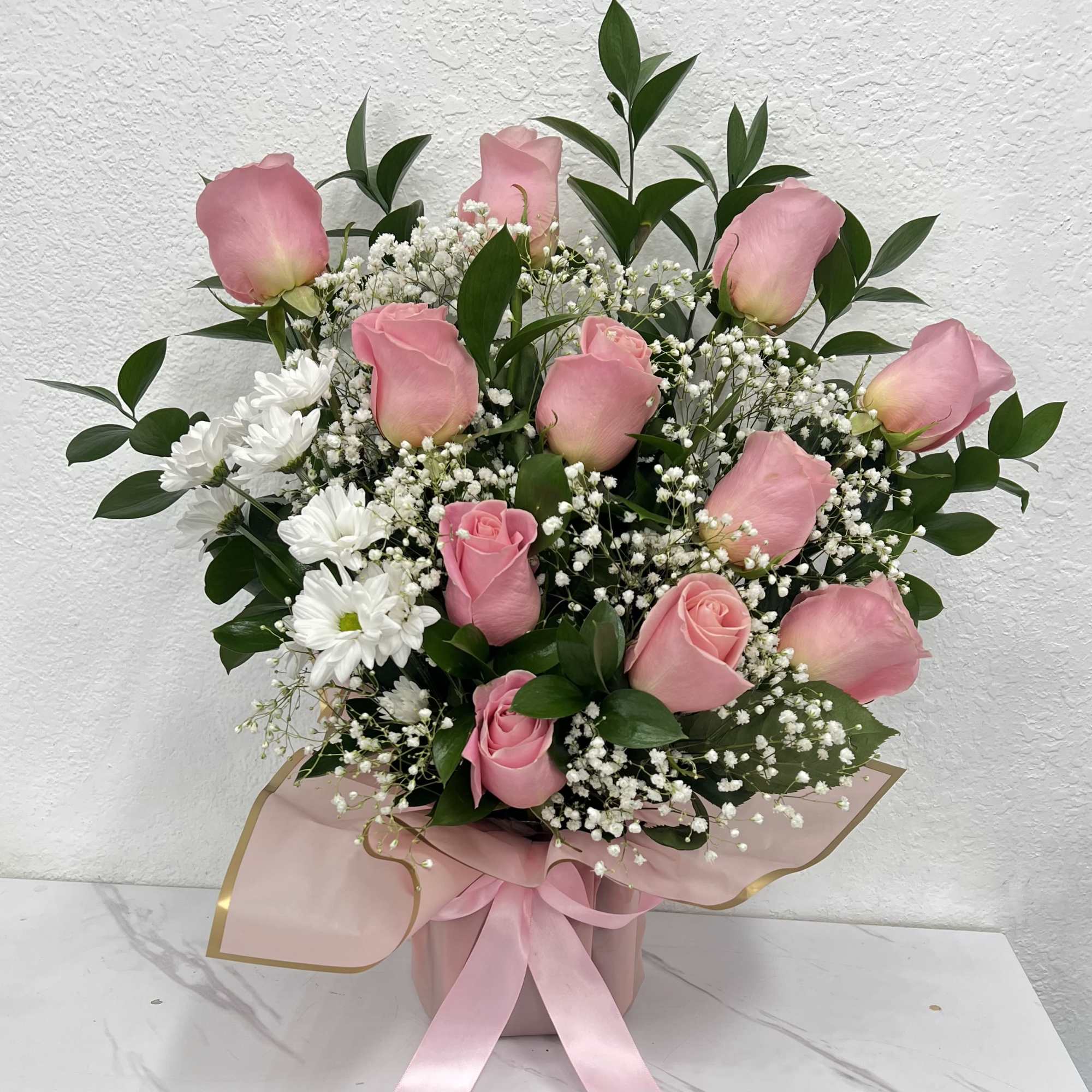 Pink roses and white daisies arranged in a pink box with ribbon.