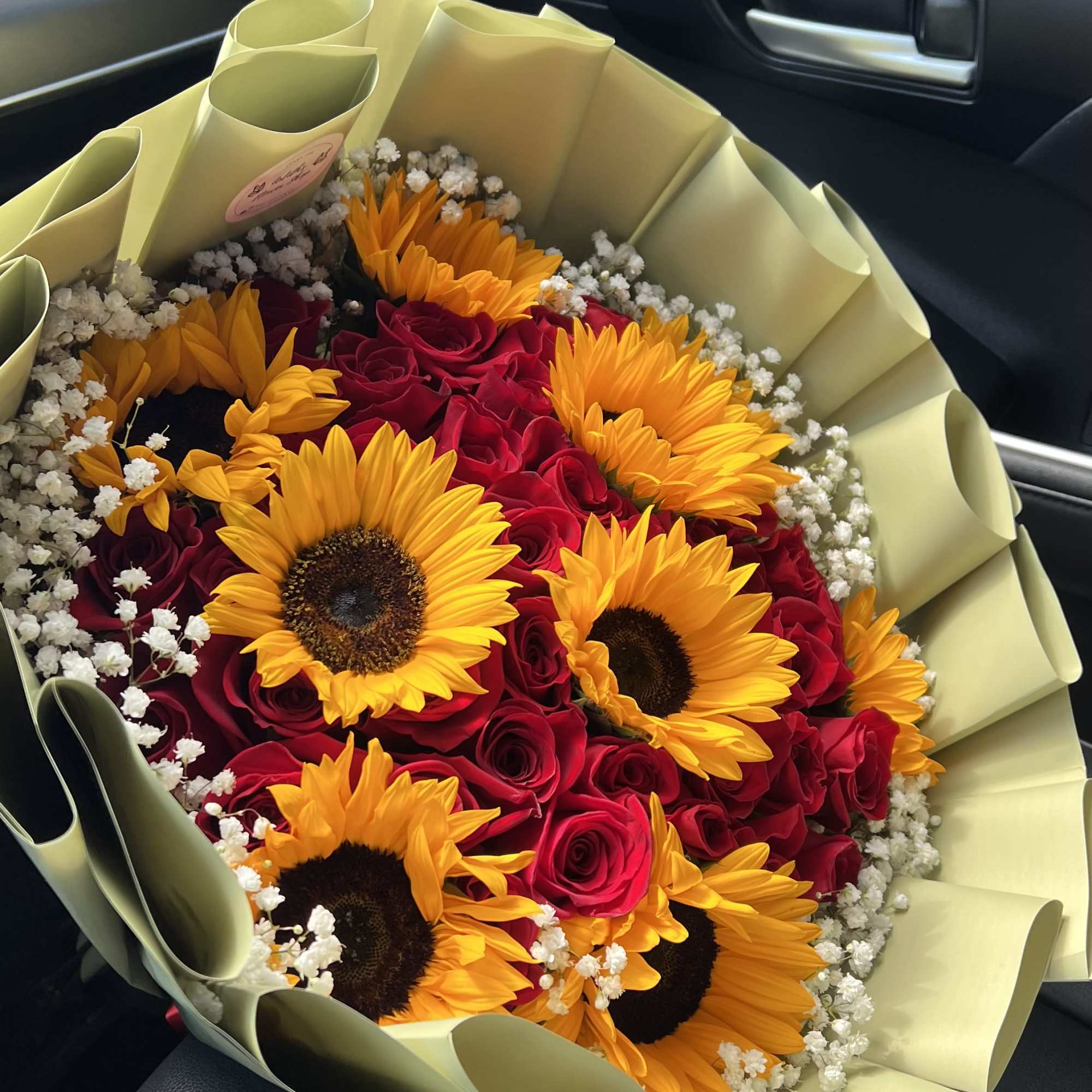Bouquet of red roses and yellow sunflowers wrapped in pale paper