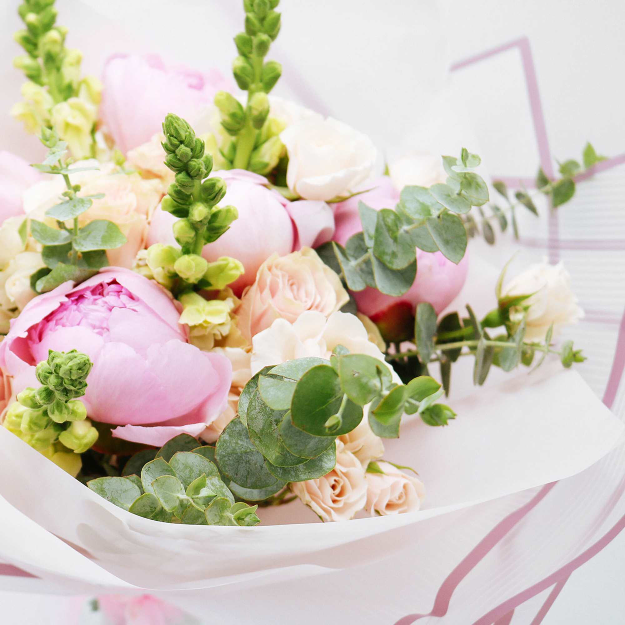 Bouquet of pink peonies and cream roses with eucalyptus in white wrapping