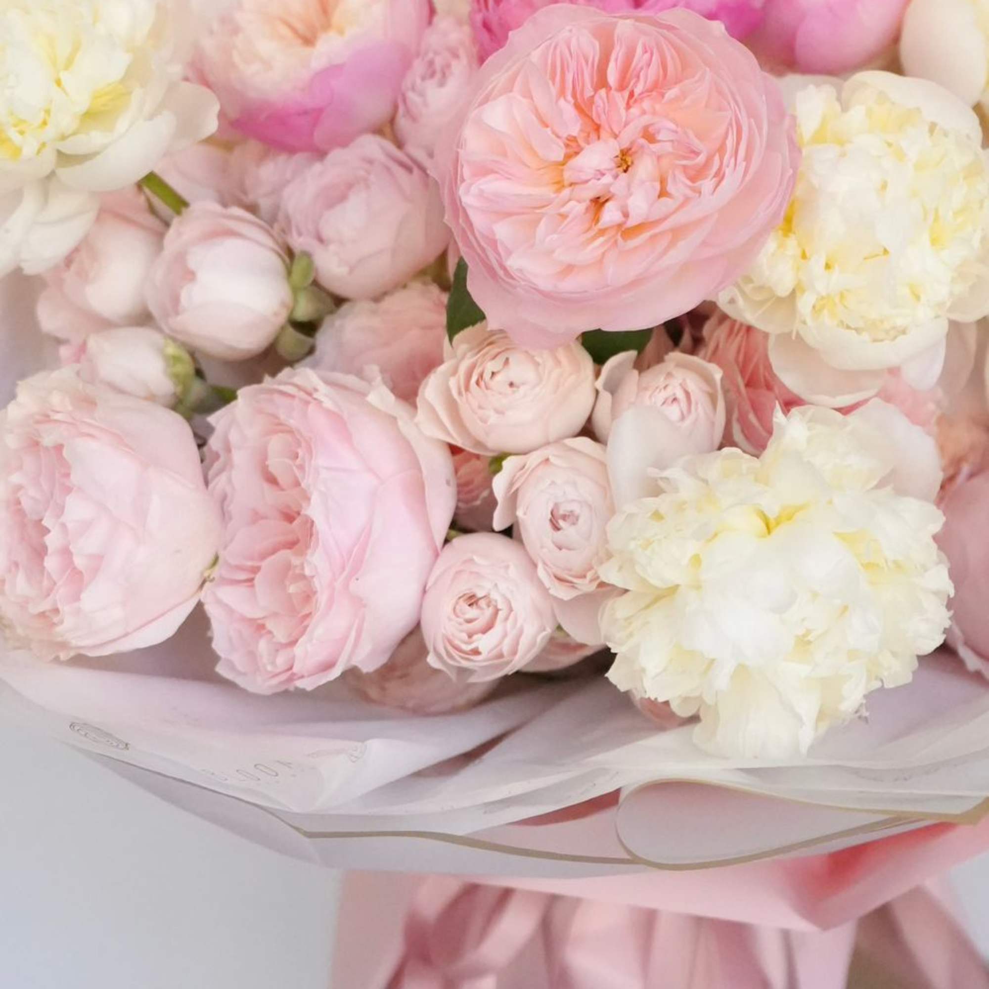 Round bouquet of pale pink and white roses and peonies in a pink hatbox with ribbons