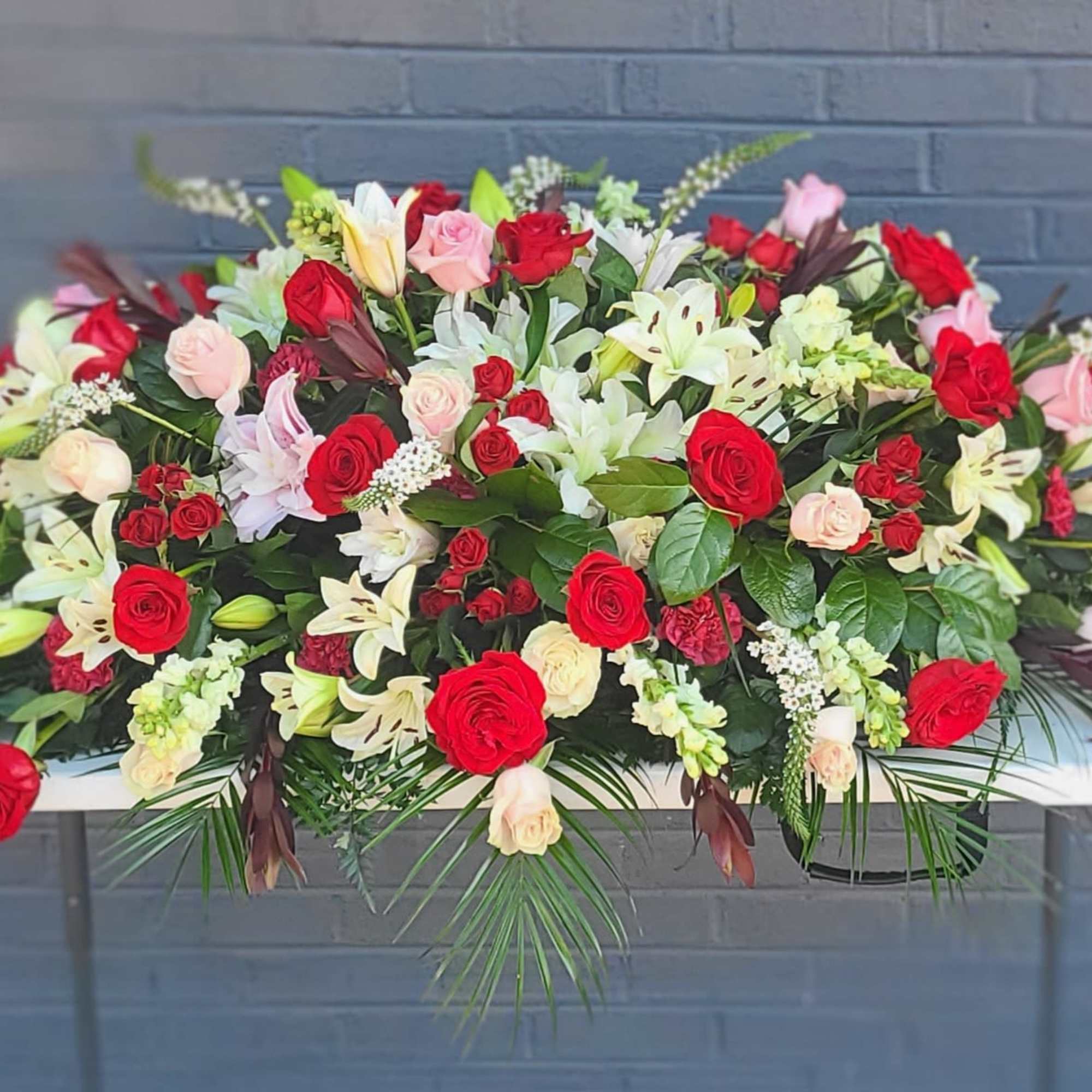 A full, formal casket spray in red, white and soft pink that