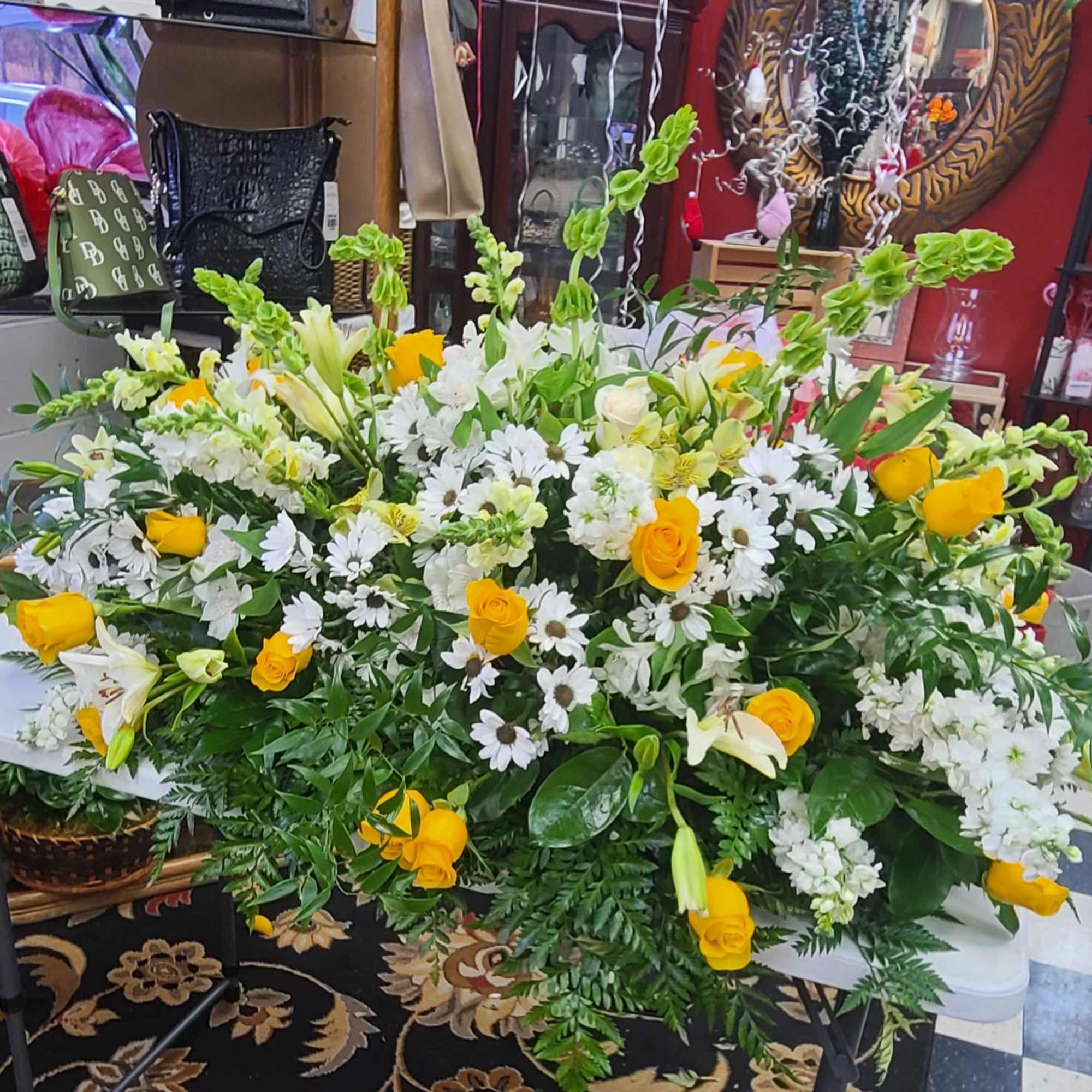 A large, elongated sympathy spray in sunny yellow and soft white that
