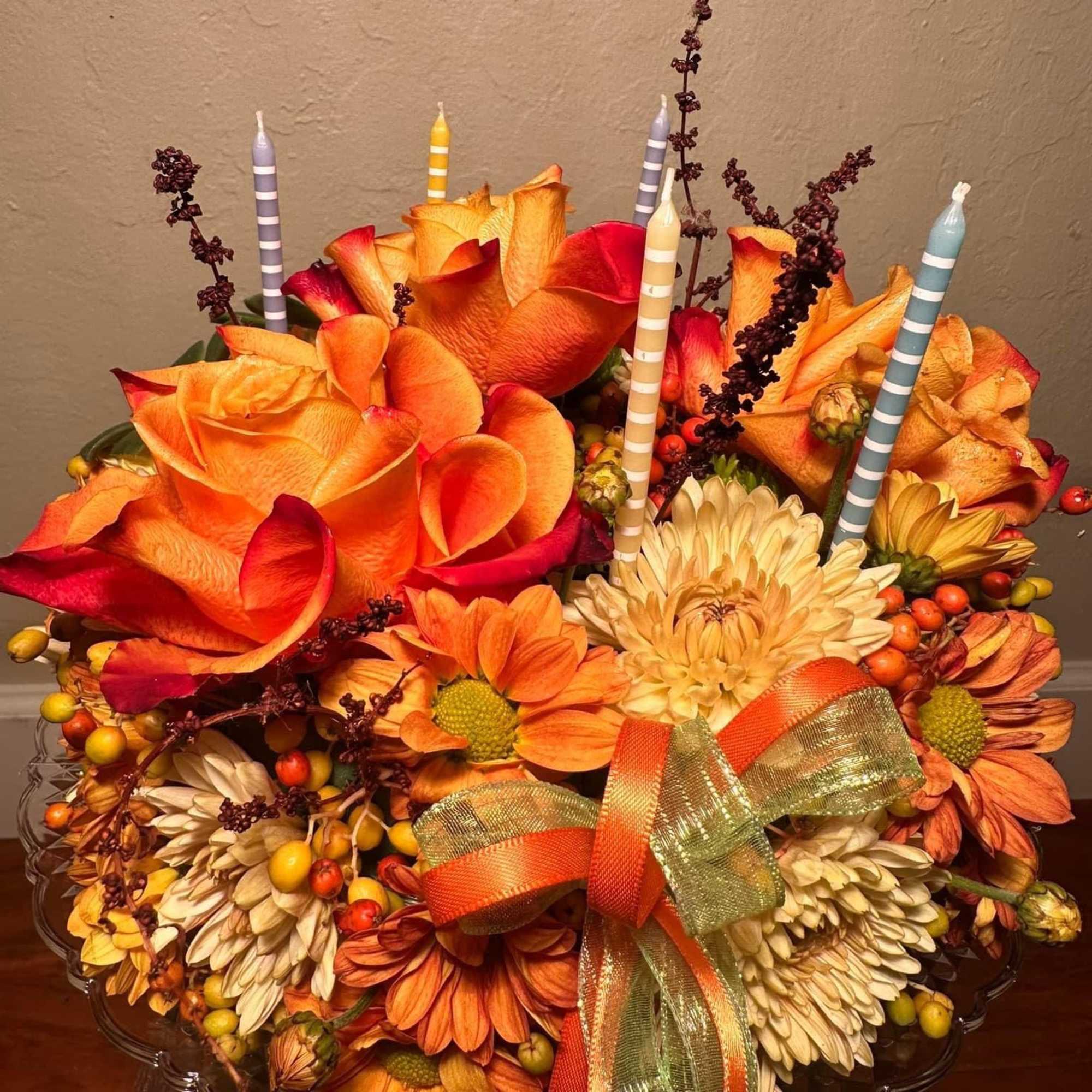 Orange roses and chrysanthemums in a clear bowl with striped candles