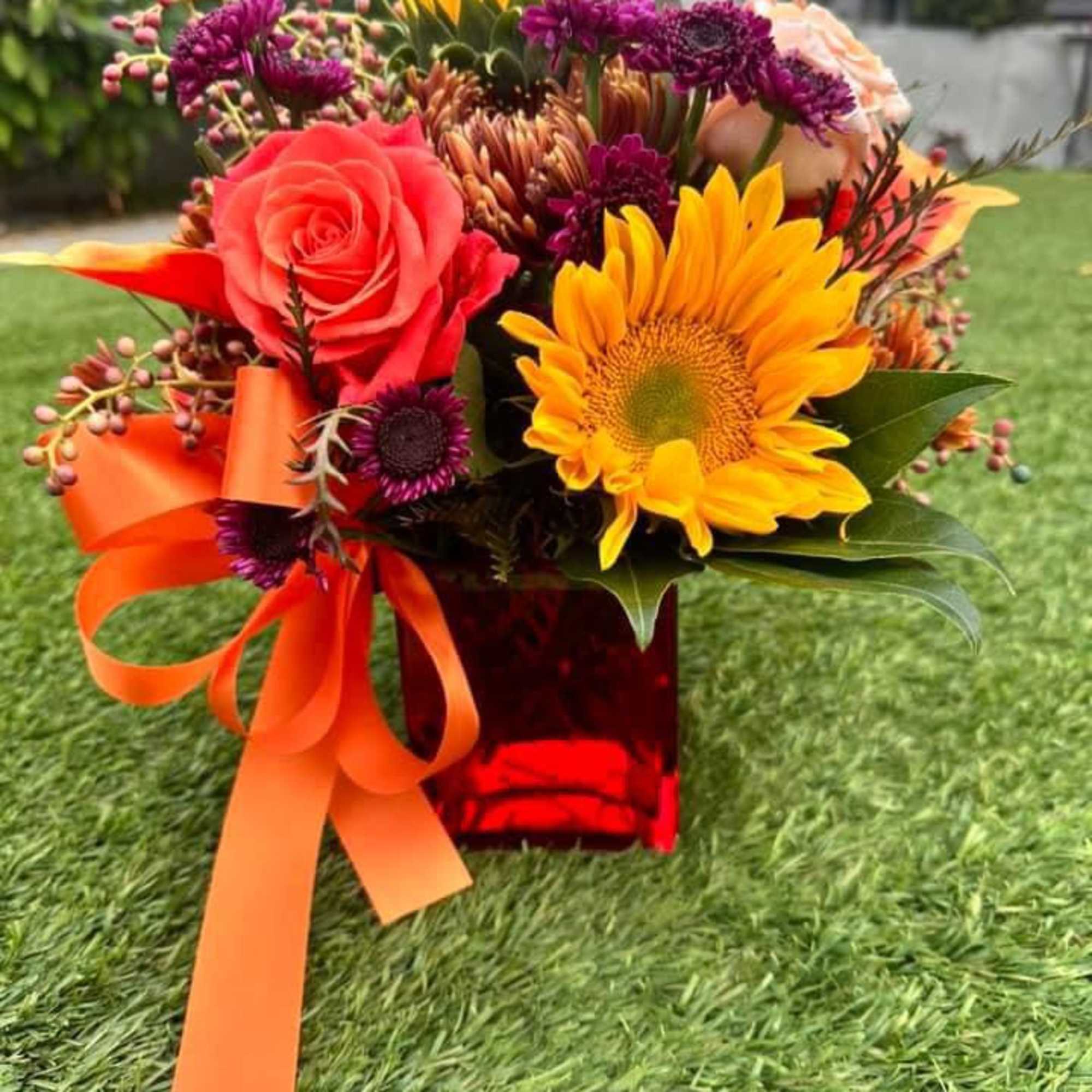 Bright mixed bouquet with sunflowers, roses, and purple mums in a red vase