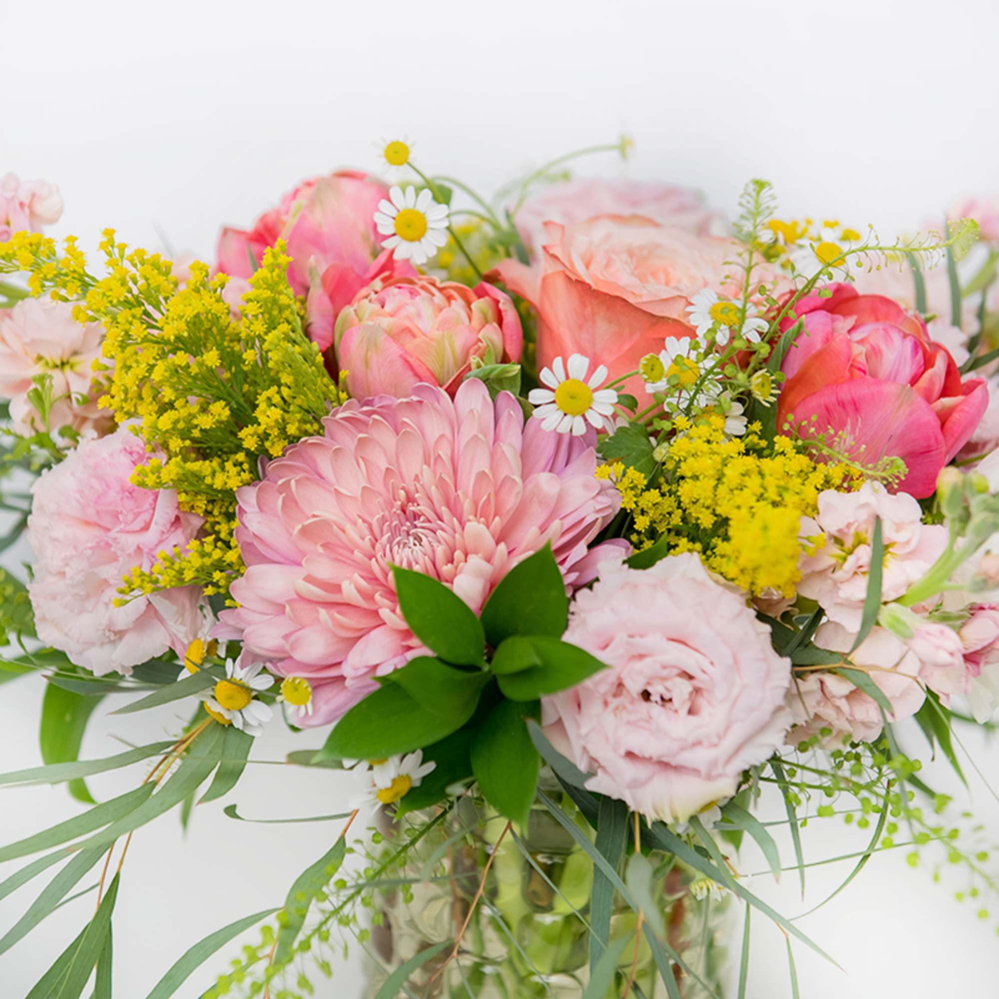 Pink and yellow mixed flower arrangement with roses, daisies, and a mum in a clear glass vase