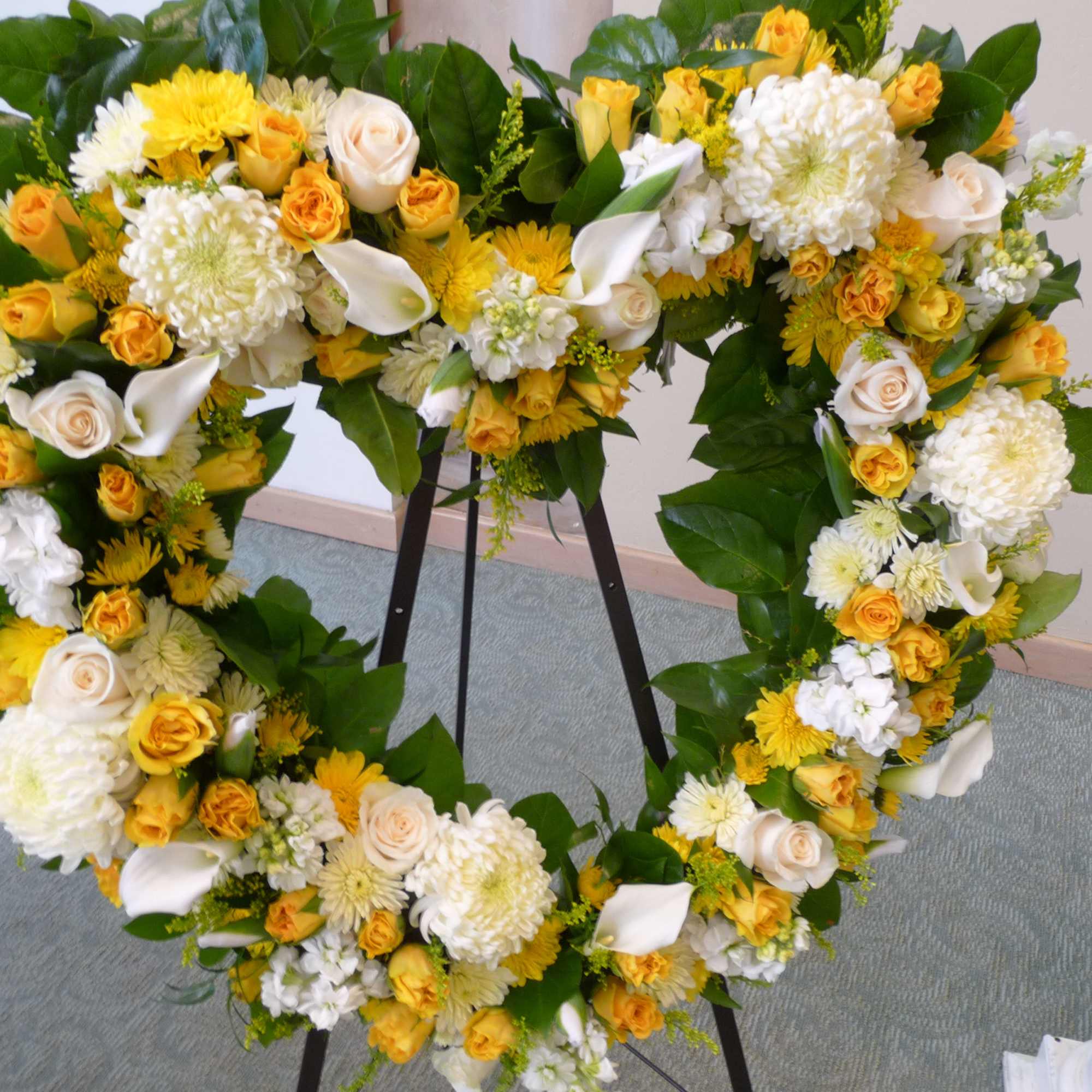 Heart-shaped floral wreath with yellow and white flowers on a stand