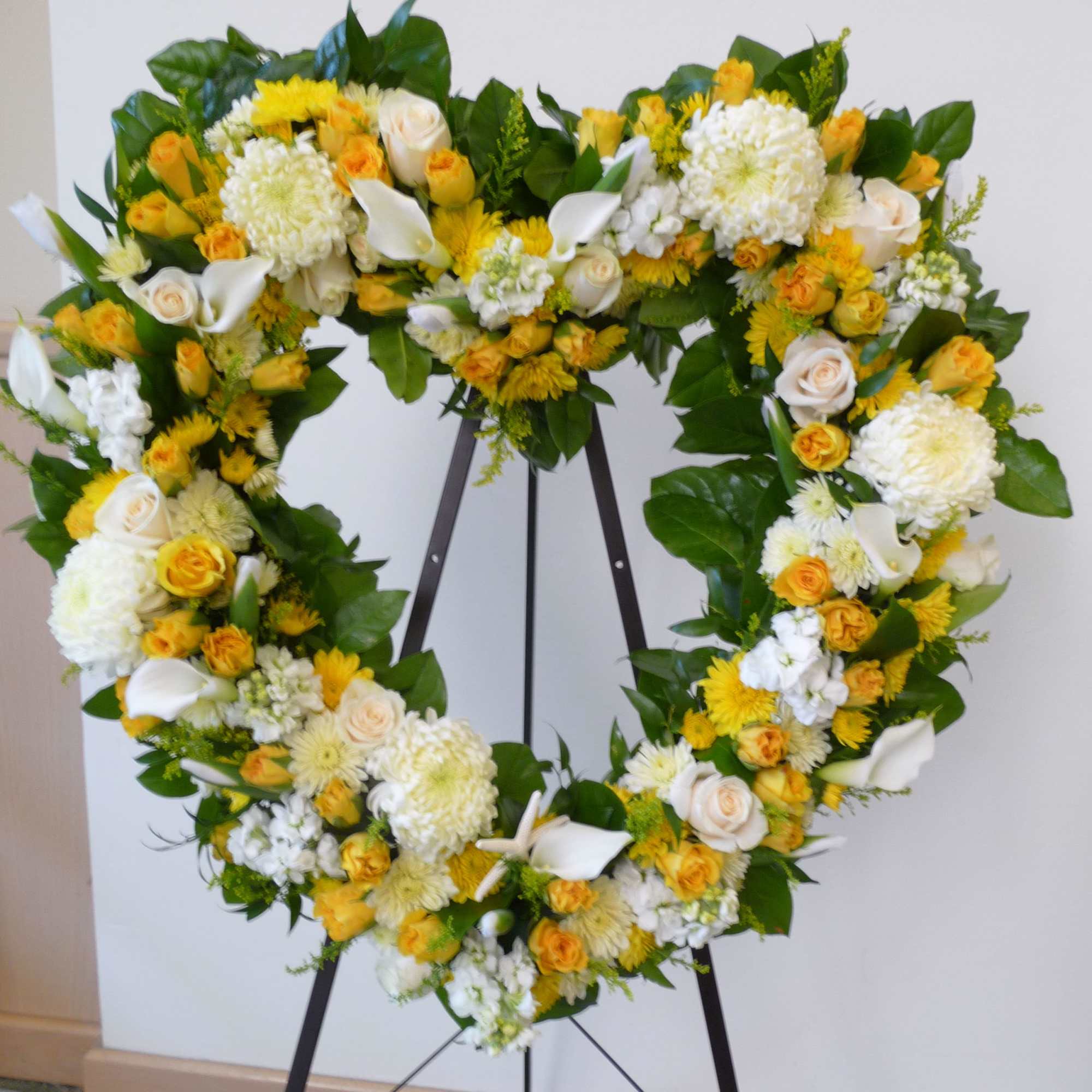 Heart-shaped floral wreath with white and yellow flowers on a stand