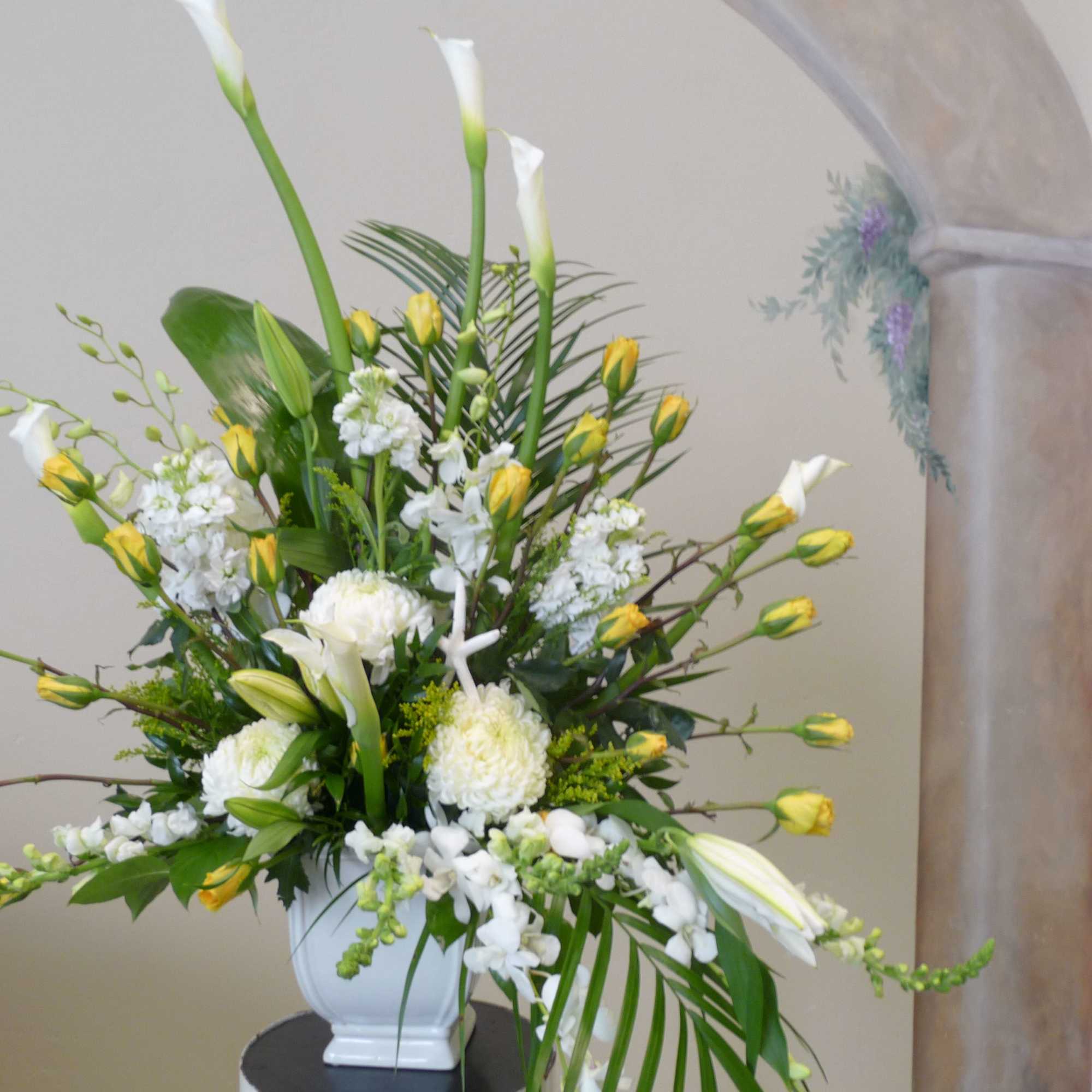Tall white floral arrangement with yellow buds in a white vase