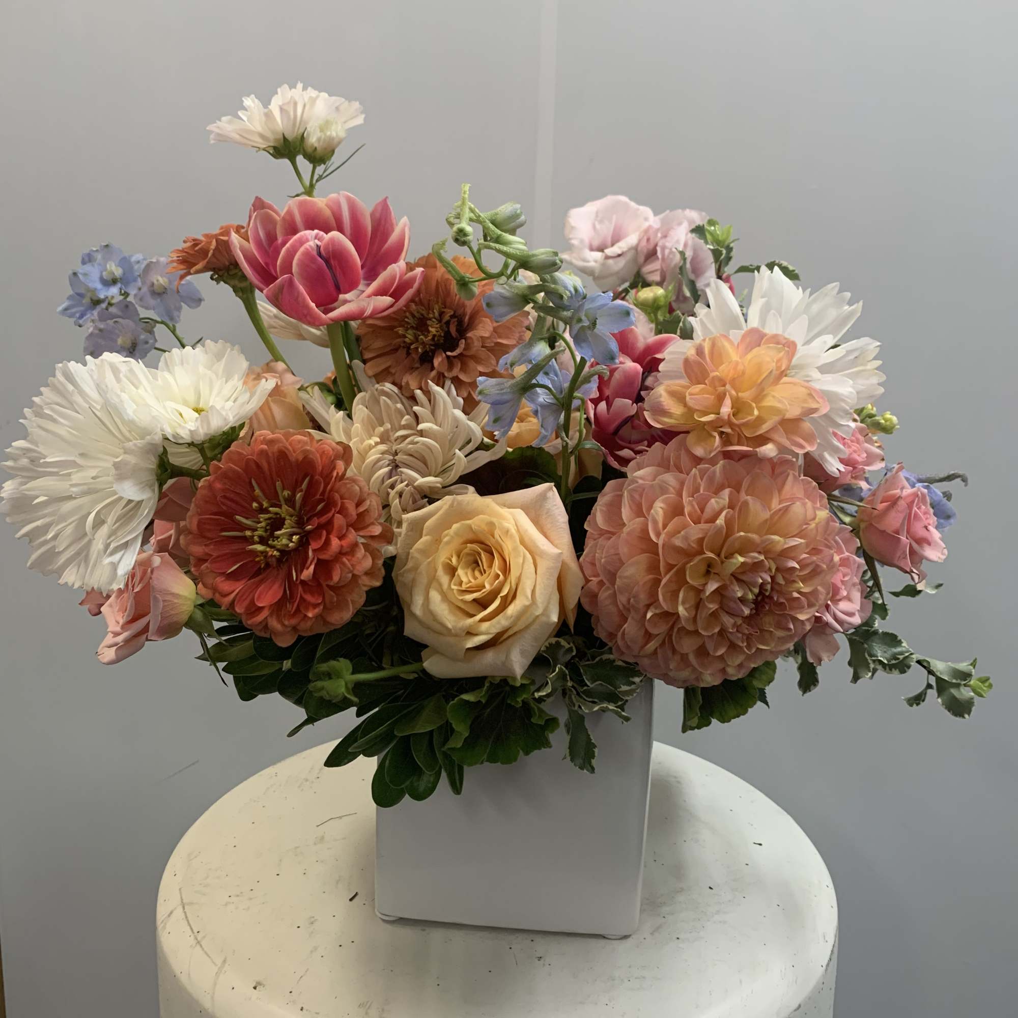 Mixed bouquet of pastel flowers in a white square vase