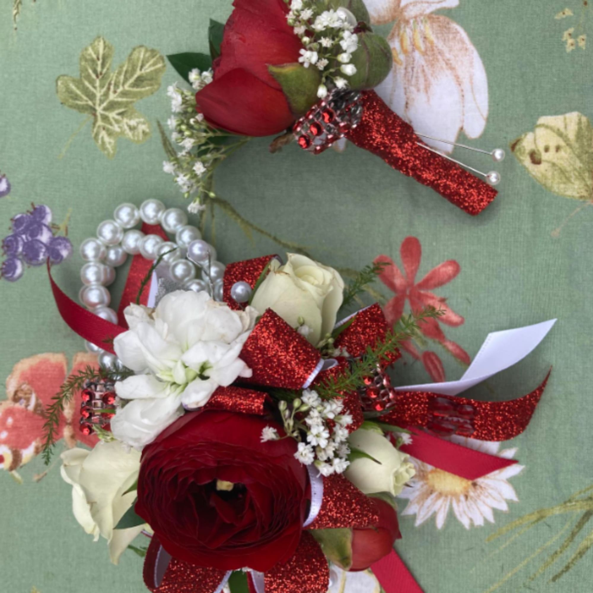 Two red and white floral boutonnieres with glittery ribbon and pearl accents