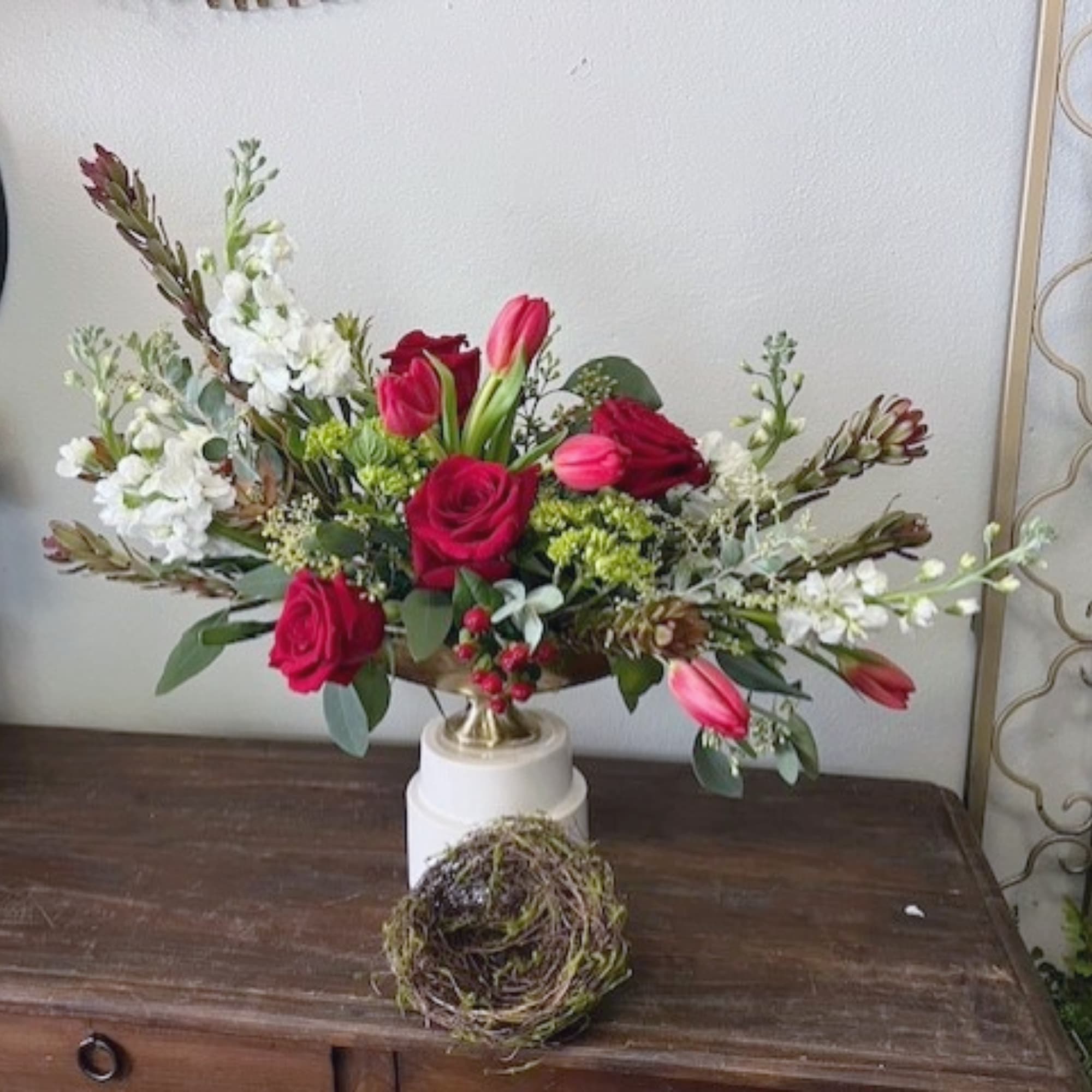 Red roses and pink tulips arranged in a white pedestal vase
