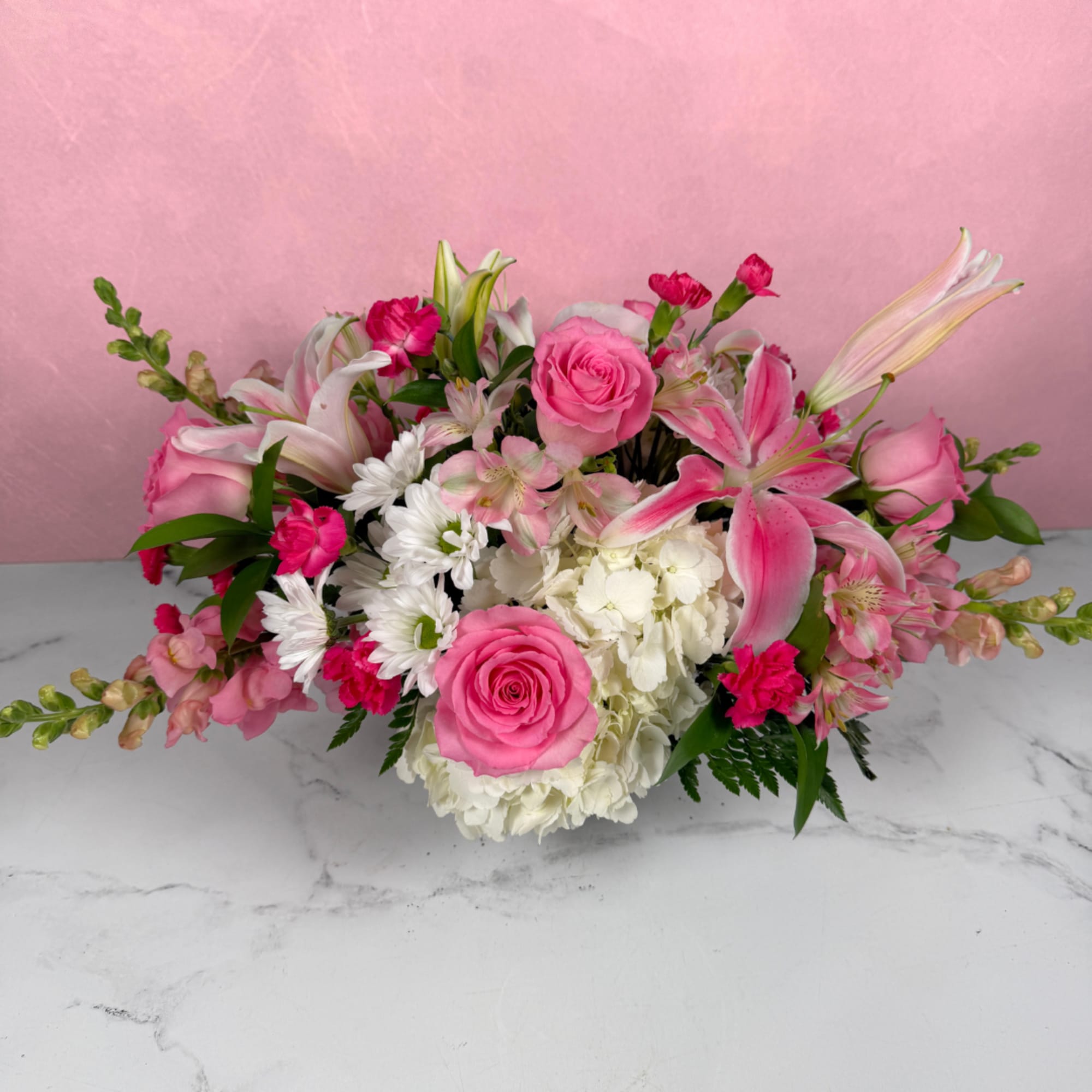 Low pink and white floral arrangement with roses, lilies, hydrangea, and daisies in a rectangular container