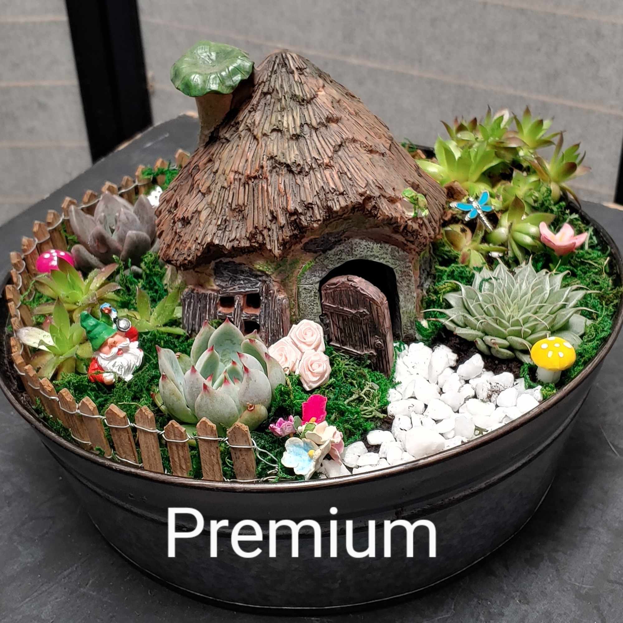 Succulent fairy garden in a round black planter with a tiny house and decorations