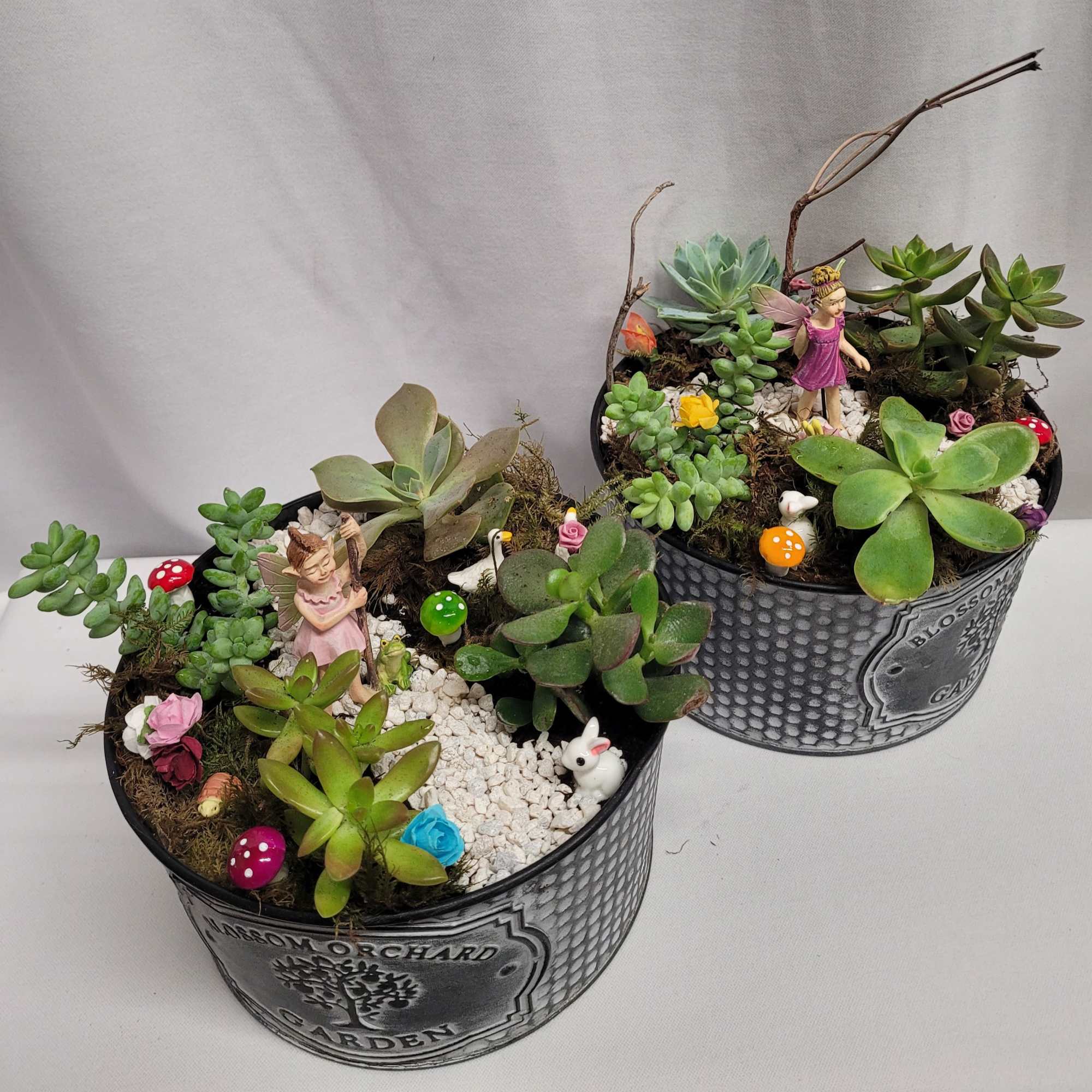 Two succulent planters with fairy figurines and small decorative mushrooms